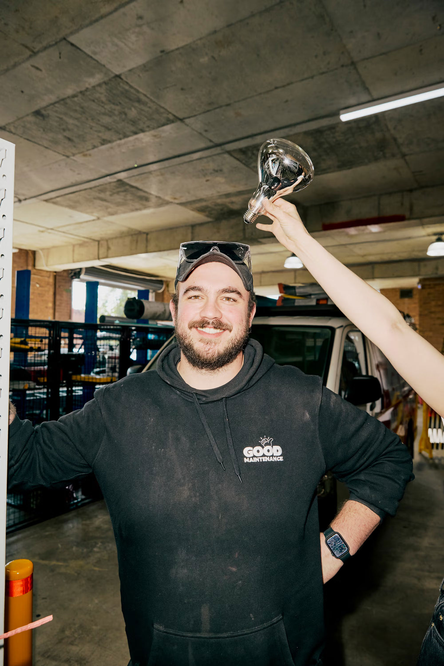 Technician smiling while a colleague holds a heat lamp above his head in the workshop.