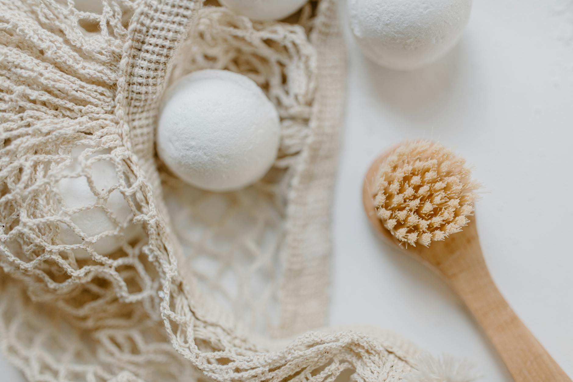 Image of bath bombs and a wooden body brush with a mesh bag for a natural body care routine.