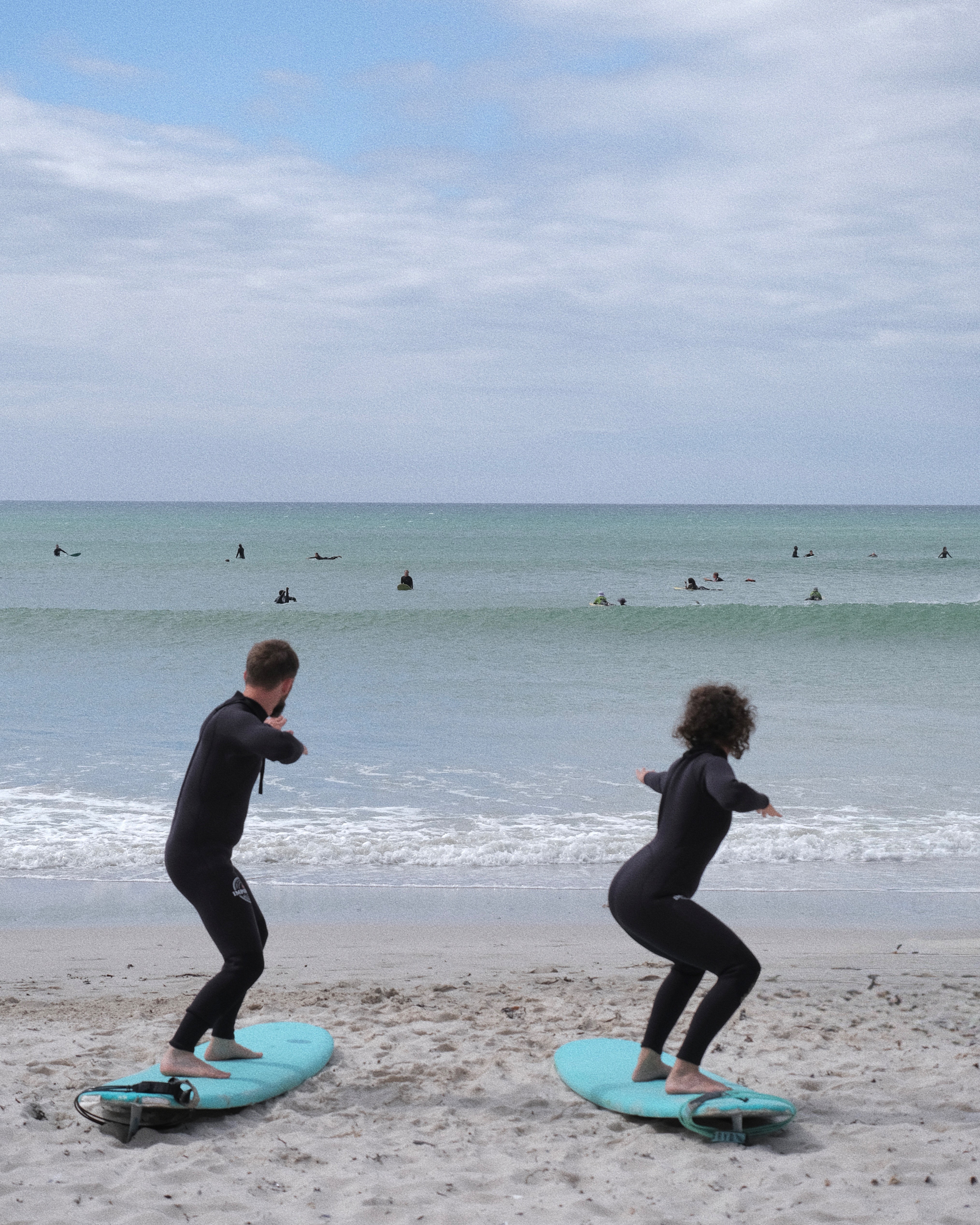 Two surf students during a twin surf lesson practicing their pop up at Muizenberg beach in Cape Town