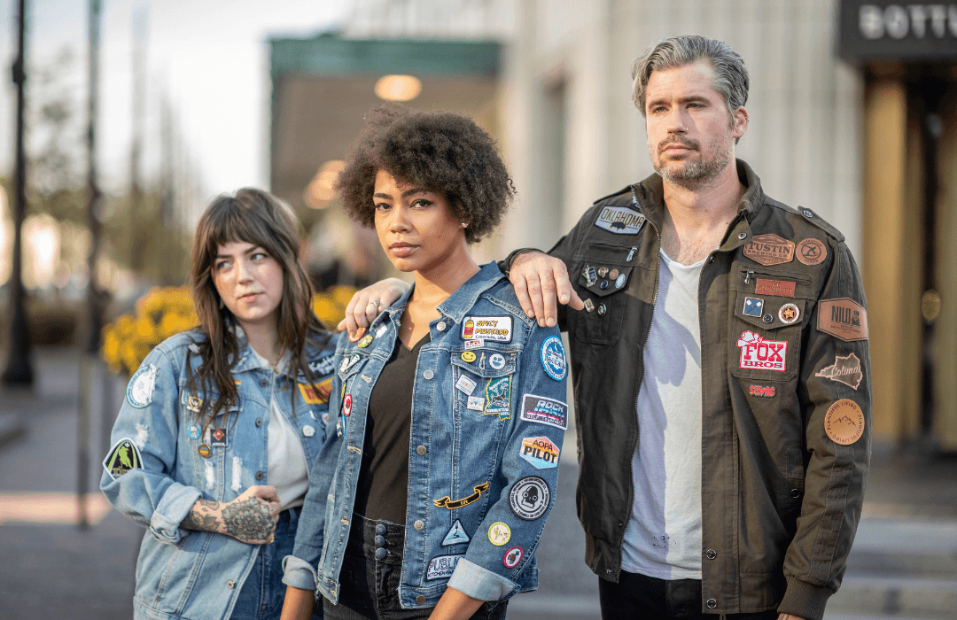 3 Models wearing jackets with patches on them. Two women are on the left wearing denim jacketsand there is a man on the right wearing an olive green canvas jacket.