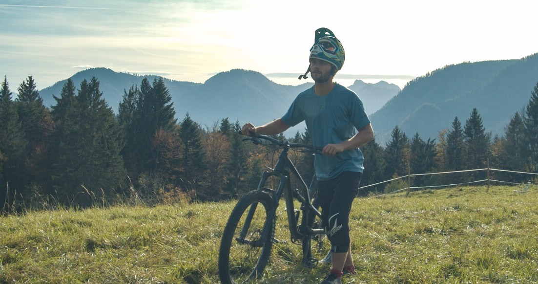 Mountain biker on a meadow in morning light in front of the pre-alpine ridges — the core of the region is not high alpine but the transition from flatland to mountains