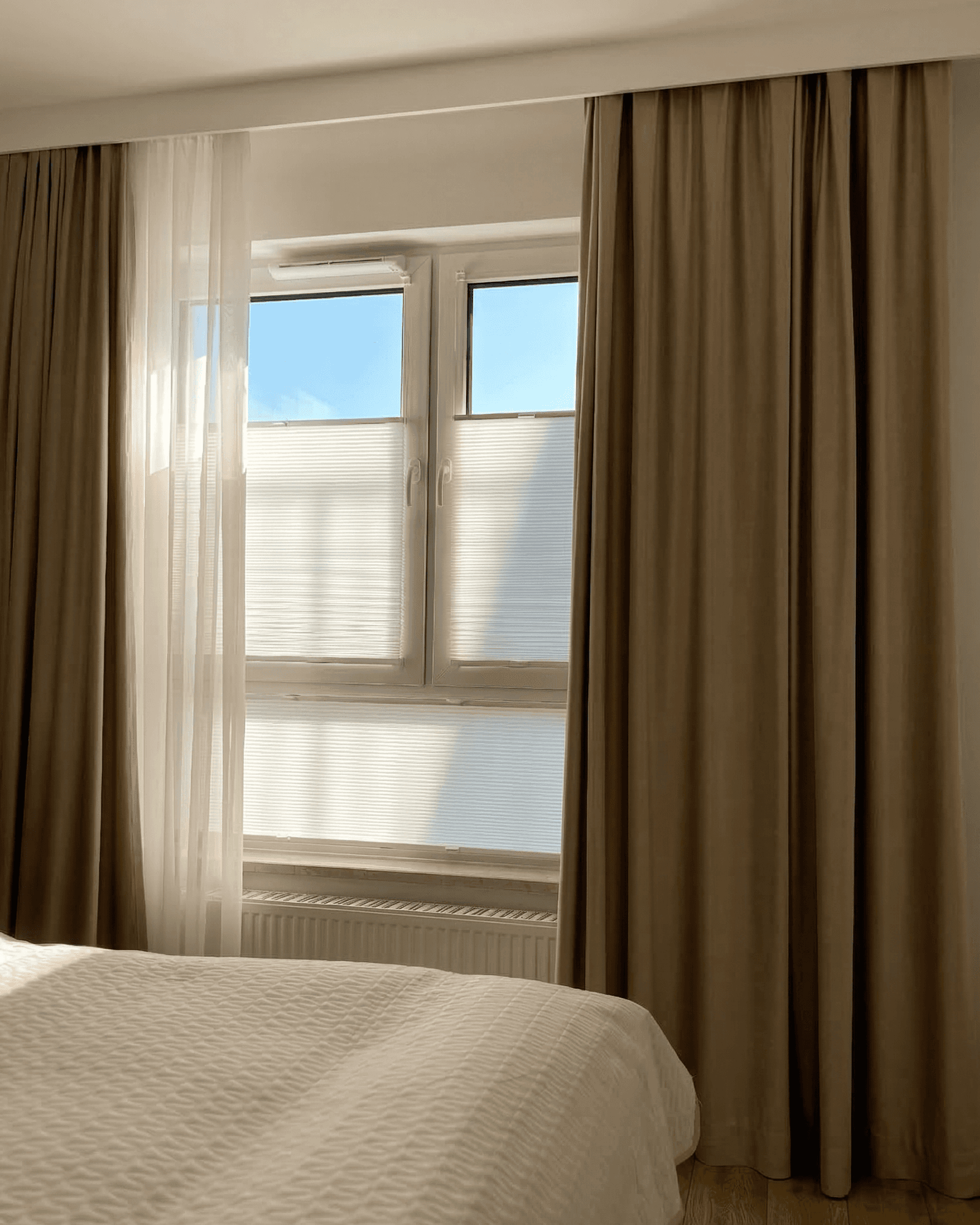 Piękne brązowe zasłony w sypialni, a na oknie estetyczne i delikatnie jasne plisy.