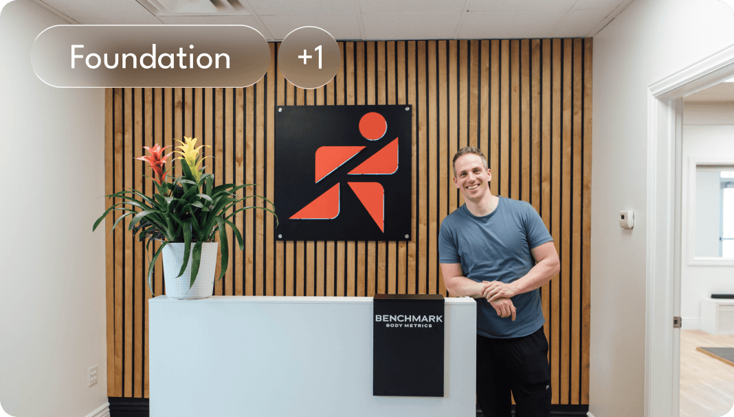 A dark glass bottle with a pump sits on a stone, surrounded by green leaves and textured background.