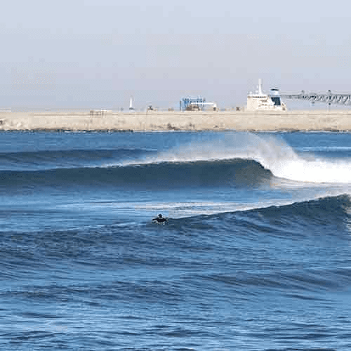 Surfer riding waves near pier – surfboard rental in ferrel