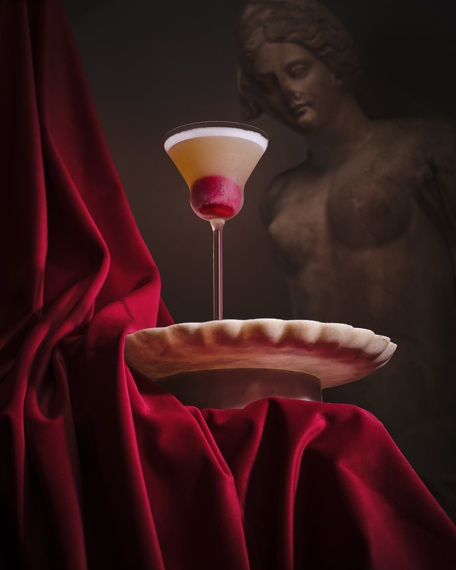 A beautifully styled cocktail glass floats above a plate, set against a rich red velvet backdrop.