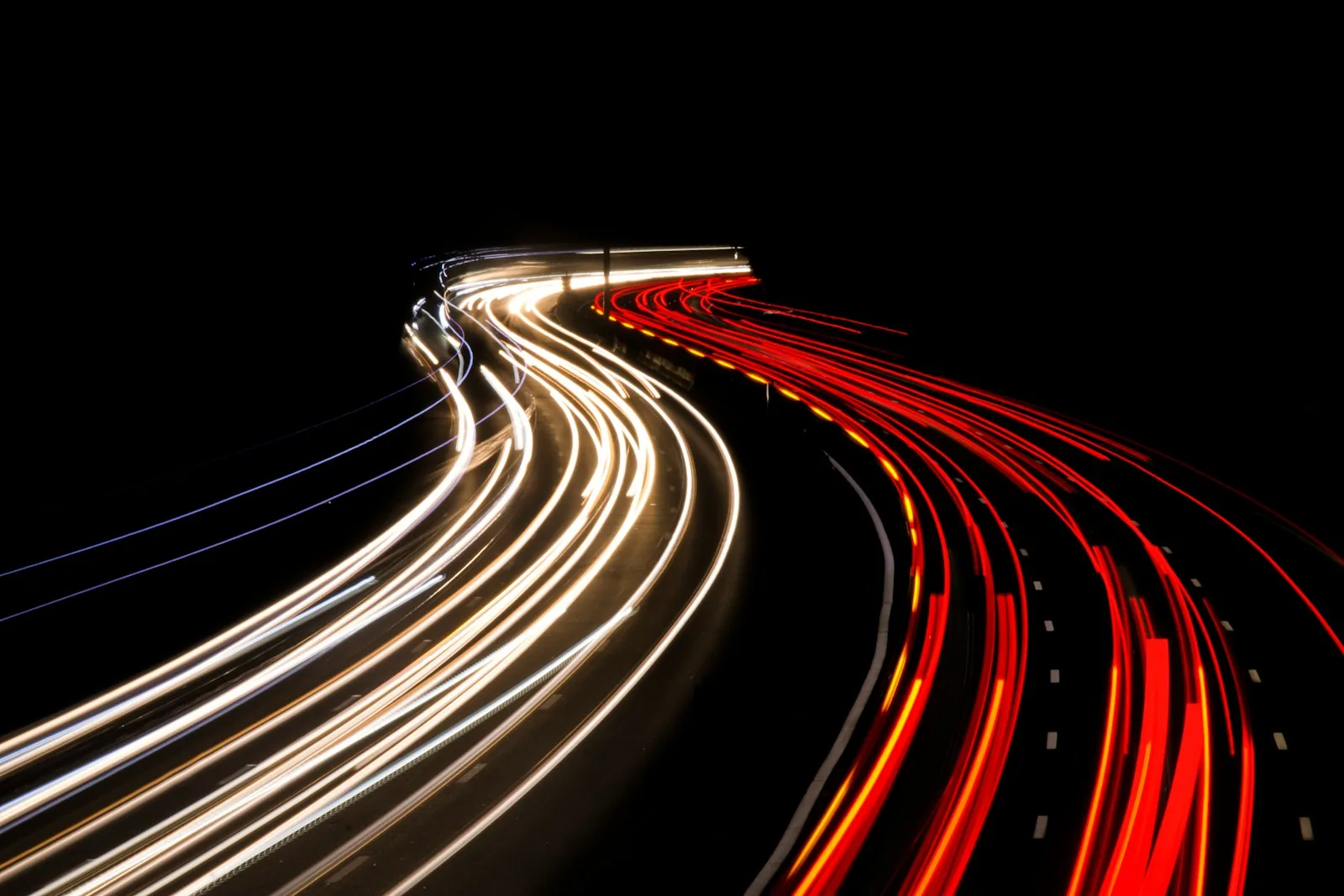 Long exposure of a curving highway at night, with white headlight trails on one side and red taillight trails on the other