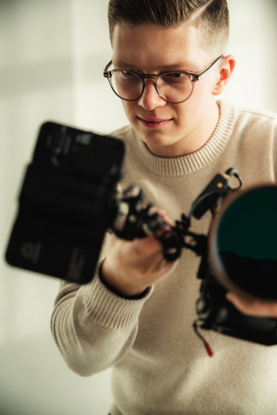 Close-up portrait of a person wearing a gray insulated hooded jacket with the hood up, showing their face framed by the hood against a light background.