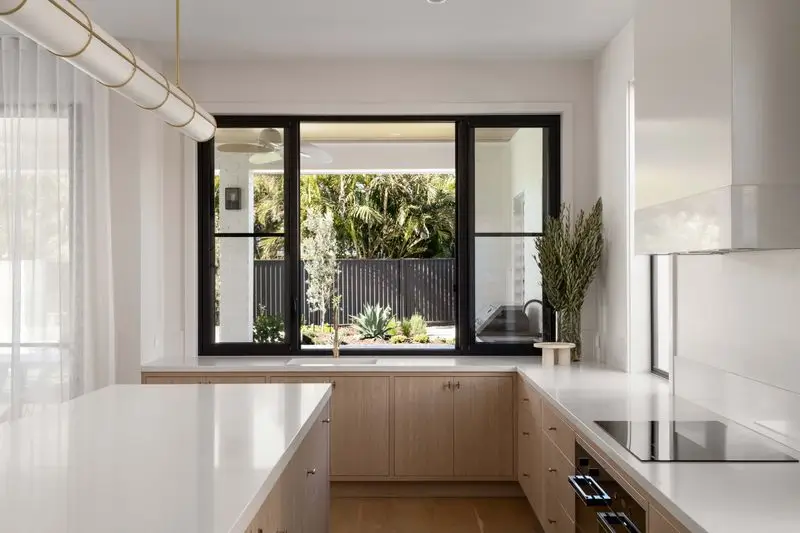 The kitchen bathed in natural light and a view of the backyrd through the window with black frame