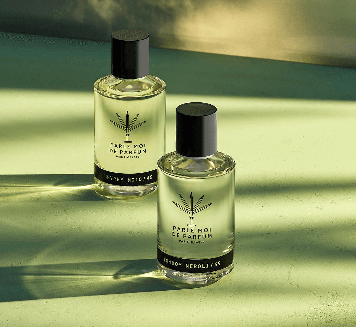Two elegant perfume bottles on a soft green surface, reflecting light, creating a serene atmosphere.