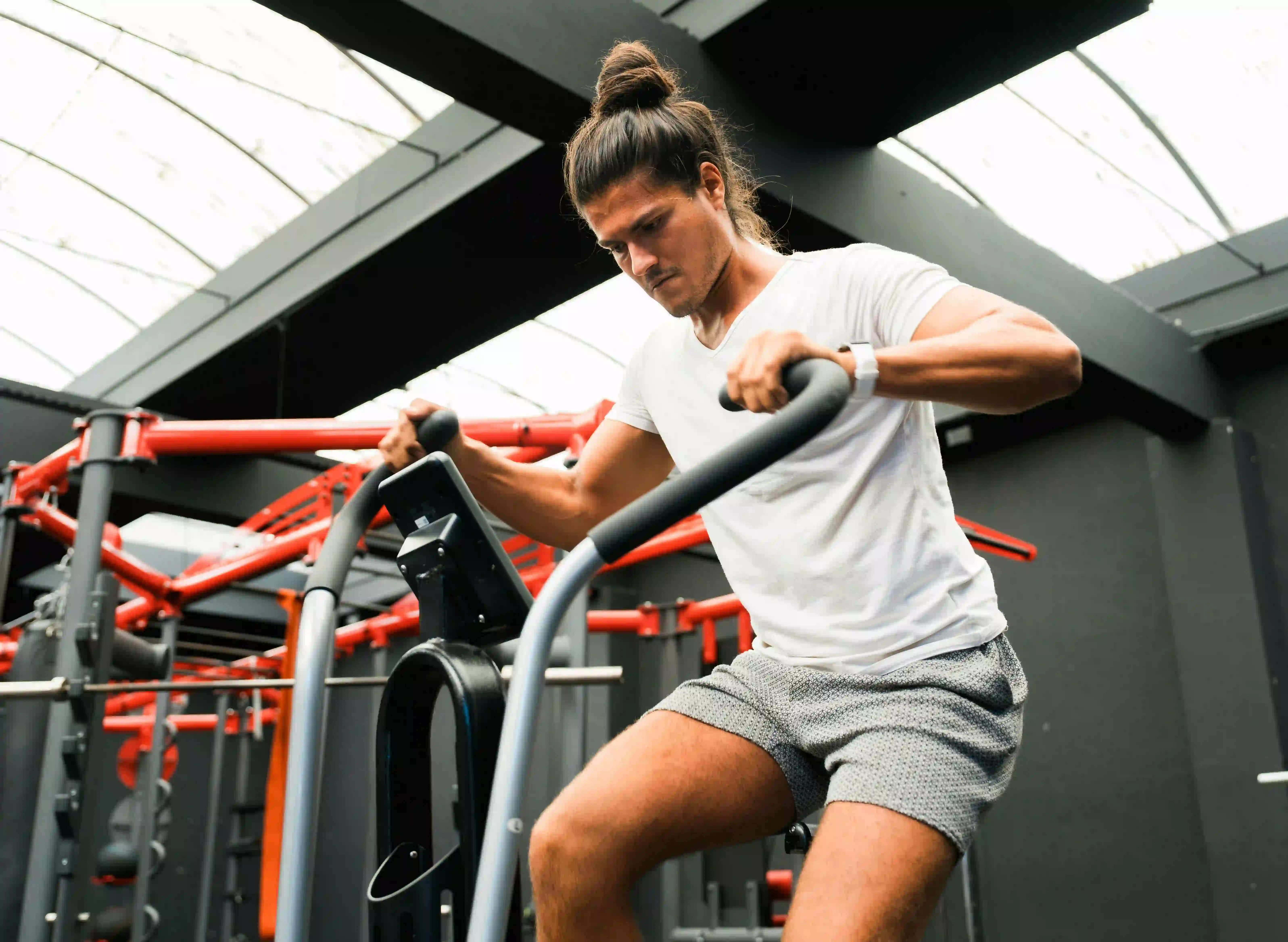 Man training on a stationary bike inside a modern gym with red metal structures.