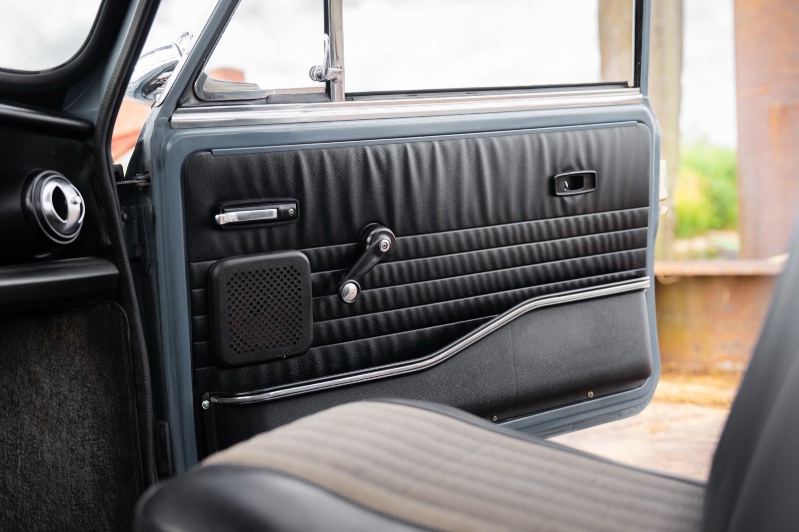 Interior view of a car door panel with sleek black upholstery and a window control mechanism. Sunlight shines in.