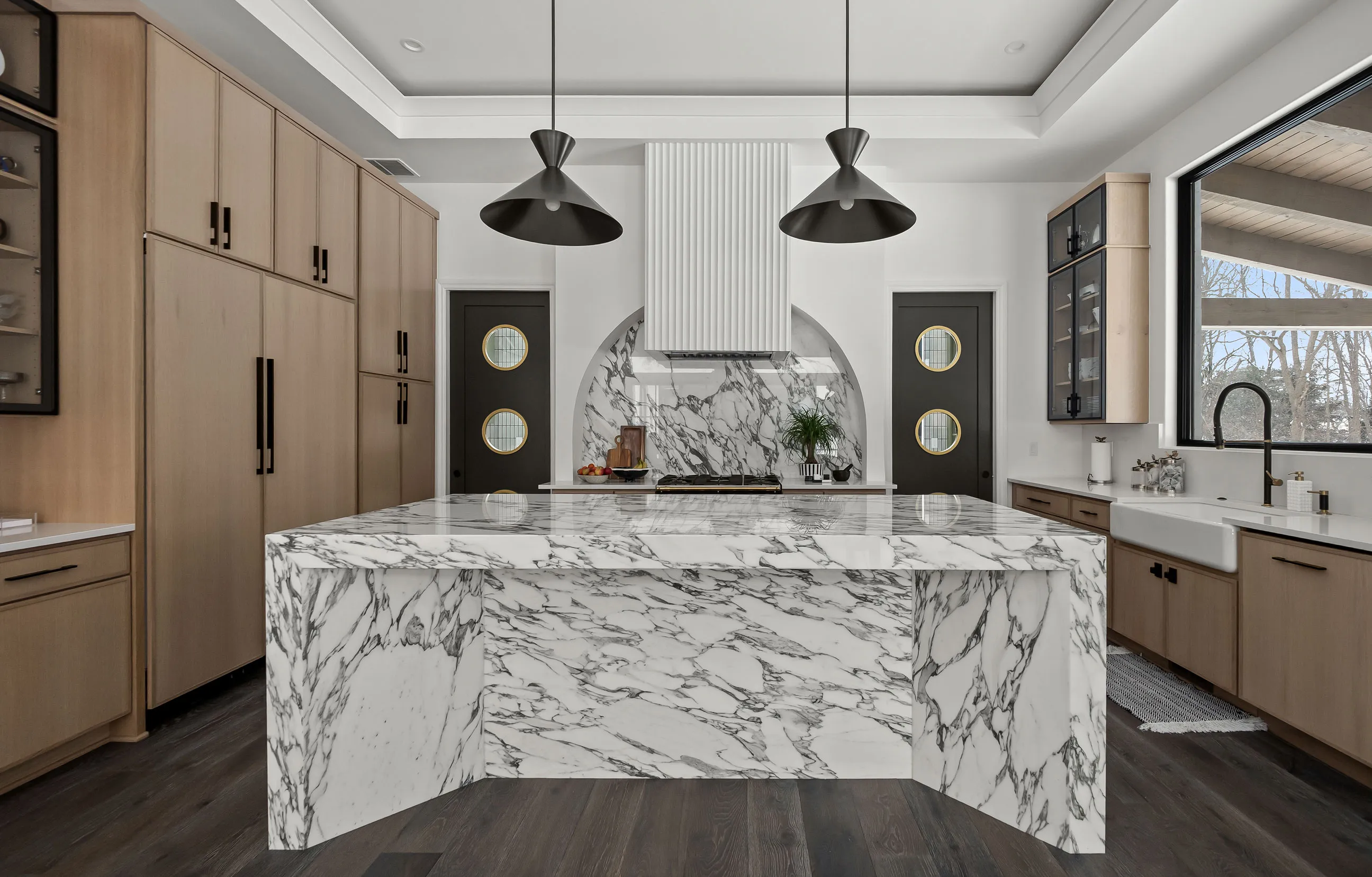 Contemporary kitchen with a dramatic marble waterfall island, light wood cabinets, and black pendant lighting, representing KSI's kitchen design work.