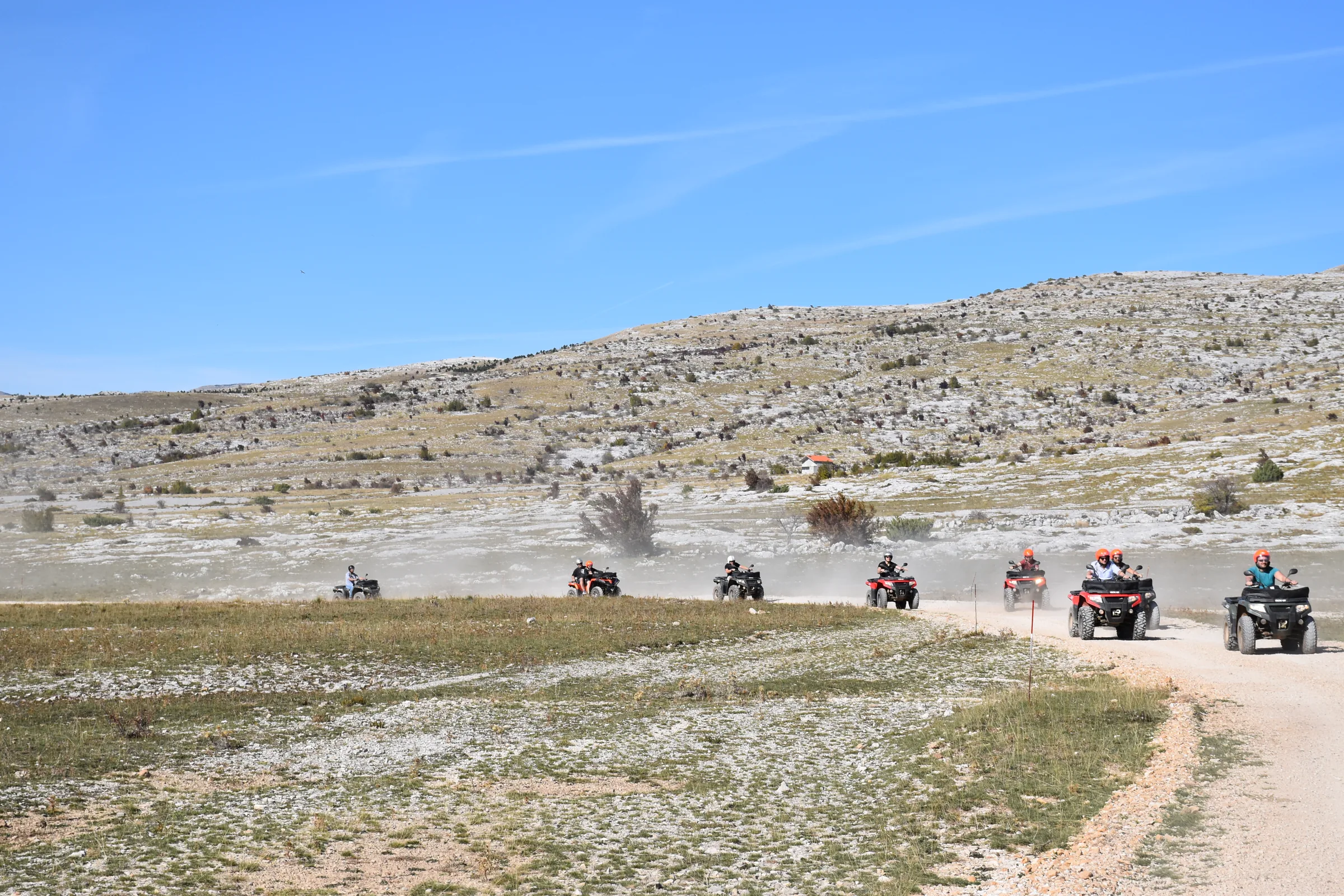Quads fahren in einer Staubwolke über eine Schotterpiste in weiter Berglandschaft