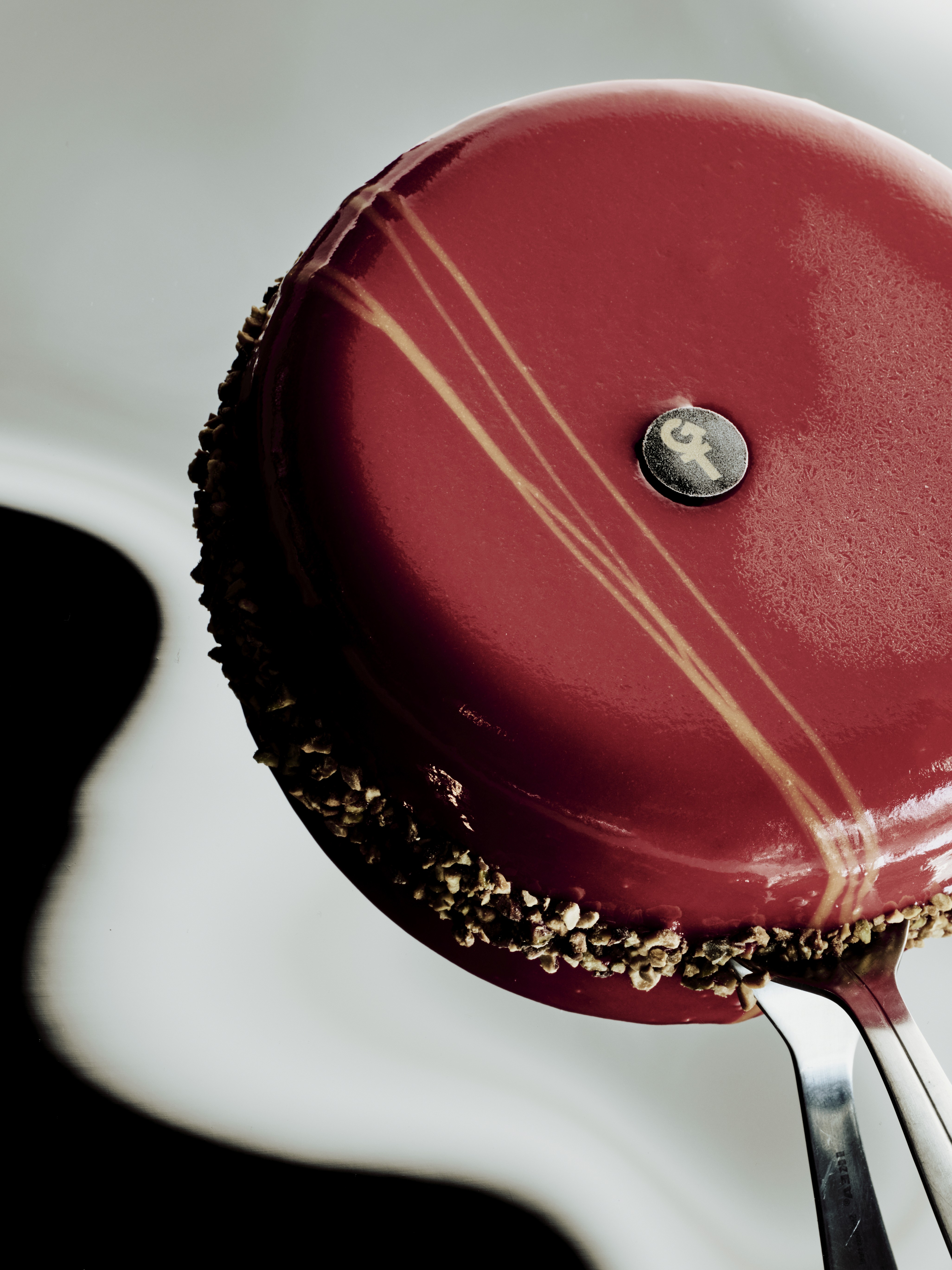 Gâteau rond glacé rouge avec filet doré et bordure croustillante, présenté sur une fourchette.