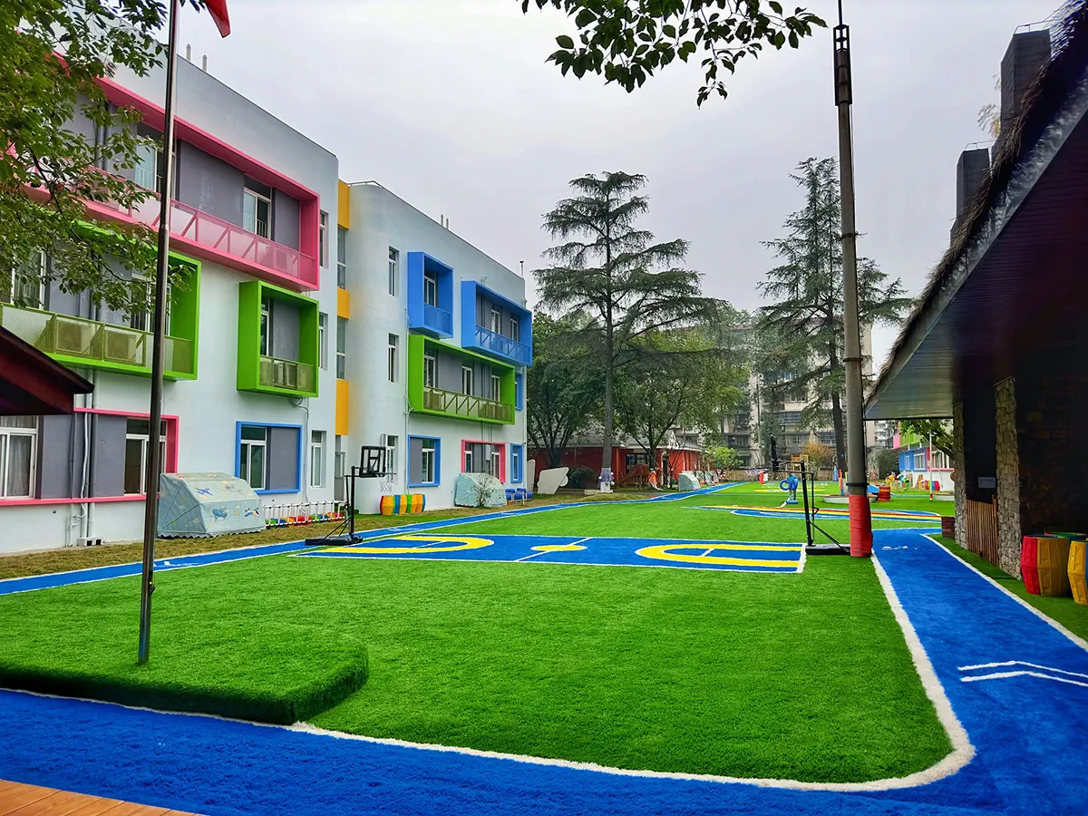 A colorful daycare school building with a spacious outdoor playground featuring artificial turf and a blue activity track
