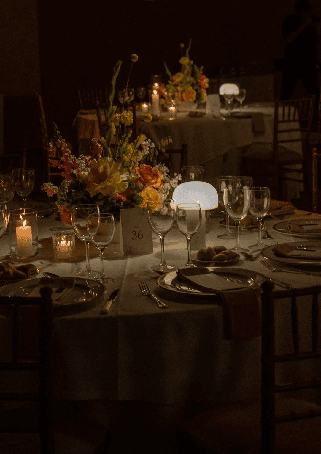 Puesta de mesa nocturna con vajilla elegante, cristalería y ambientación floral íntima para cena de boda.