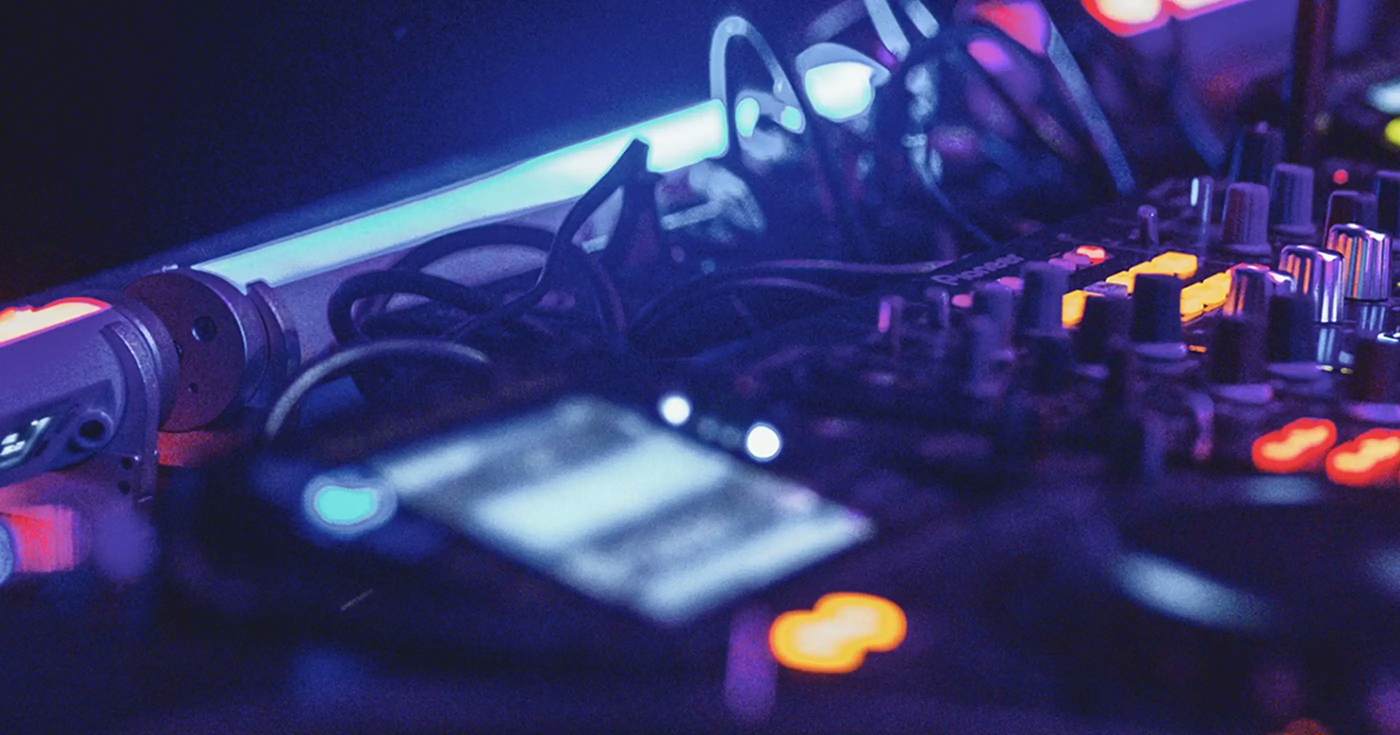 Close-up of a DJ mixer with glowing LED lights and tangled cables in a dimly lit club.