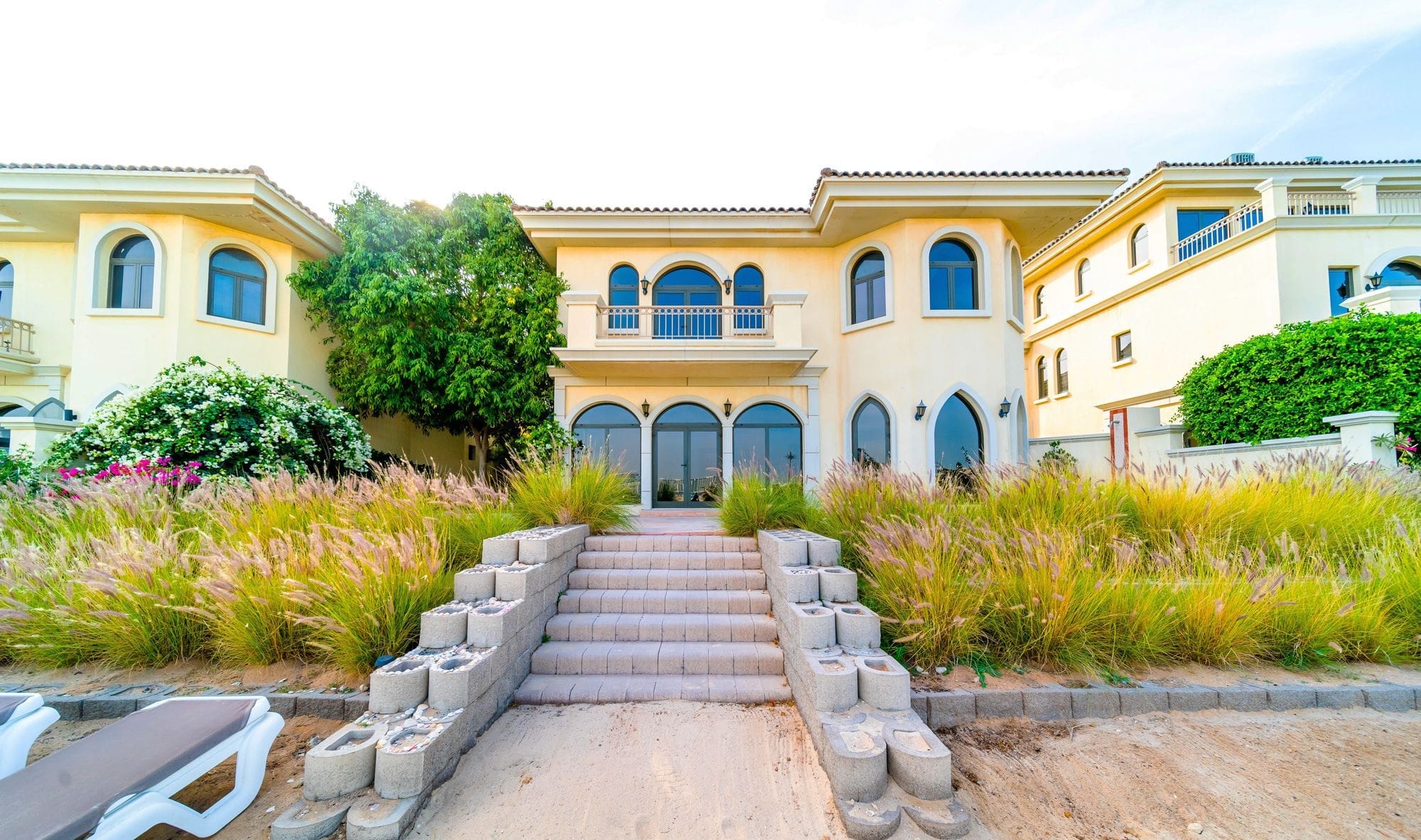 A large house with steps leading down to the beach, surrounded by garden homes and lush greenery.