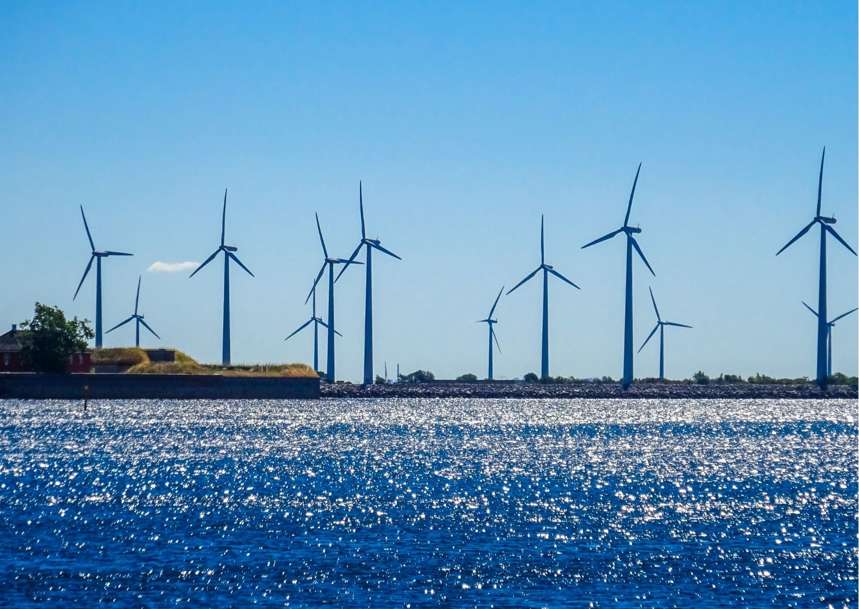 wind turbines in front of the sea with a blue sky