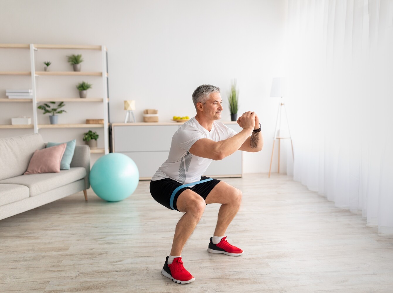 older man doing squat exercises to lose weight at home with a resistance band for added challenge