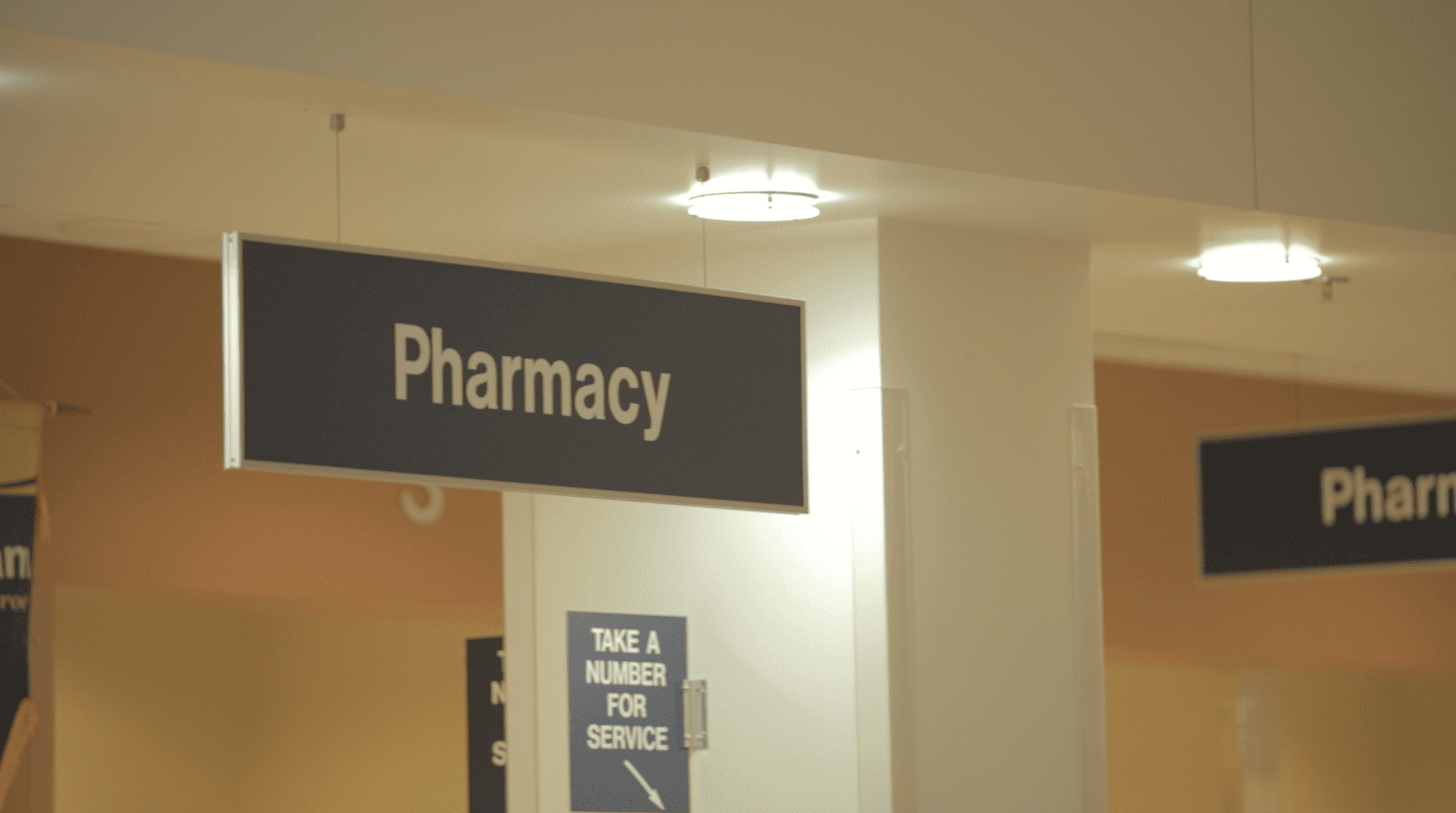 Interior of a healthcare facility showing a hanging “Pharmacy” sign—indicating a location for prescription fulfillment and patient medication services.