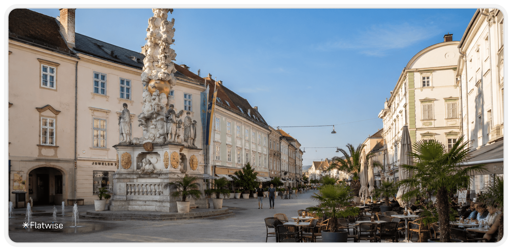 Belebter historischer Platz in Baden bei Wien mit barocker Dreifaltigkeitssäule, eleganten Altbauten und Straßencafés mit Palmen. Die Aufnahme zeigt den Platz aus einer seitlichen Perspektive in warmer Abendstimmung.