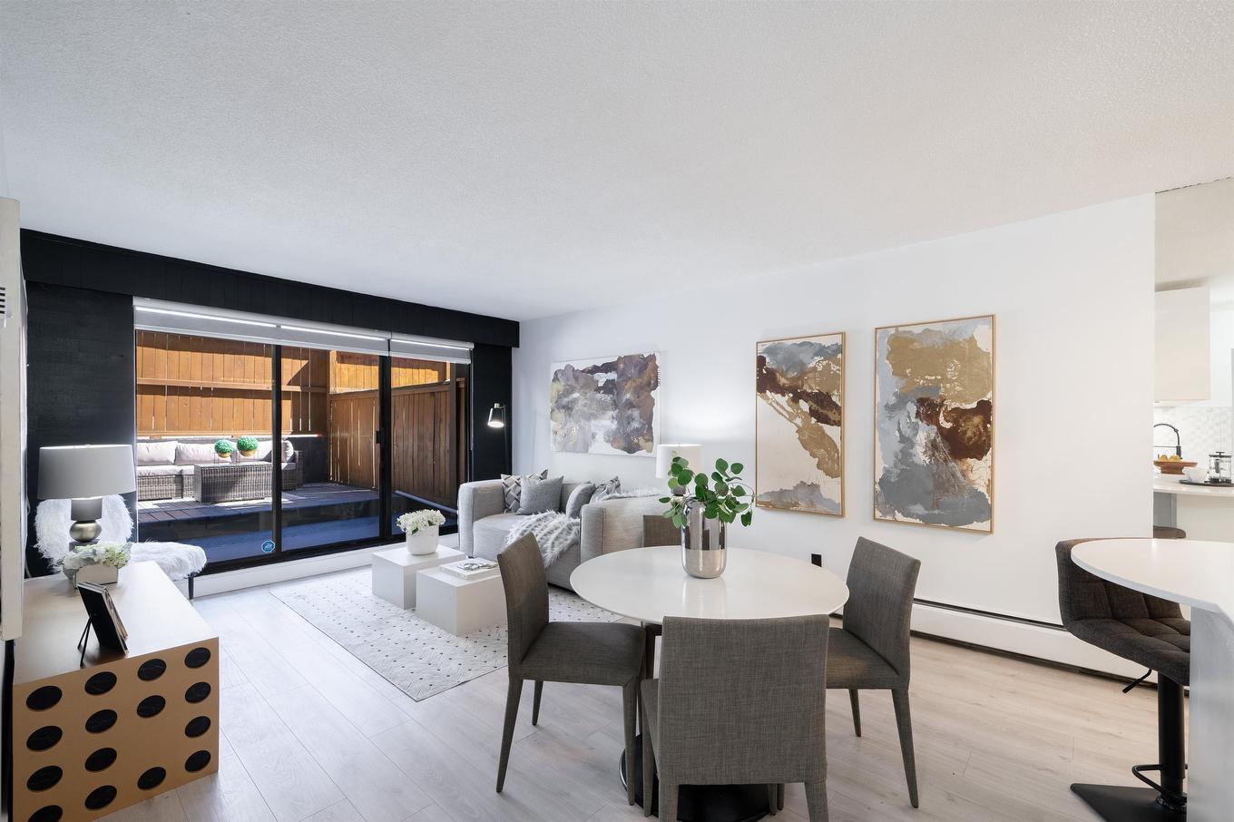 Modern living space featuring a dining area, stylish furniture, and large windows. Light colors create an airy atmosphere.