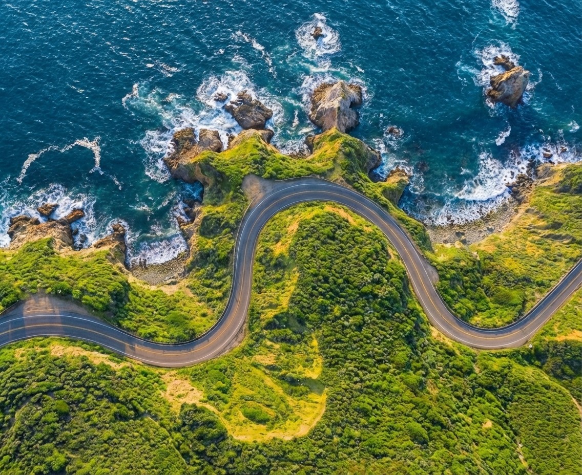 Aerial view of a winding road cutting through rocky terrain and sandy landscape.