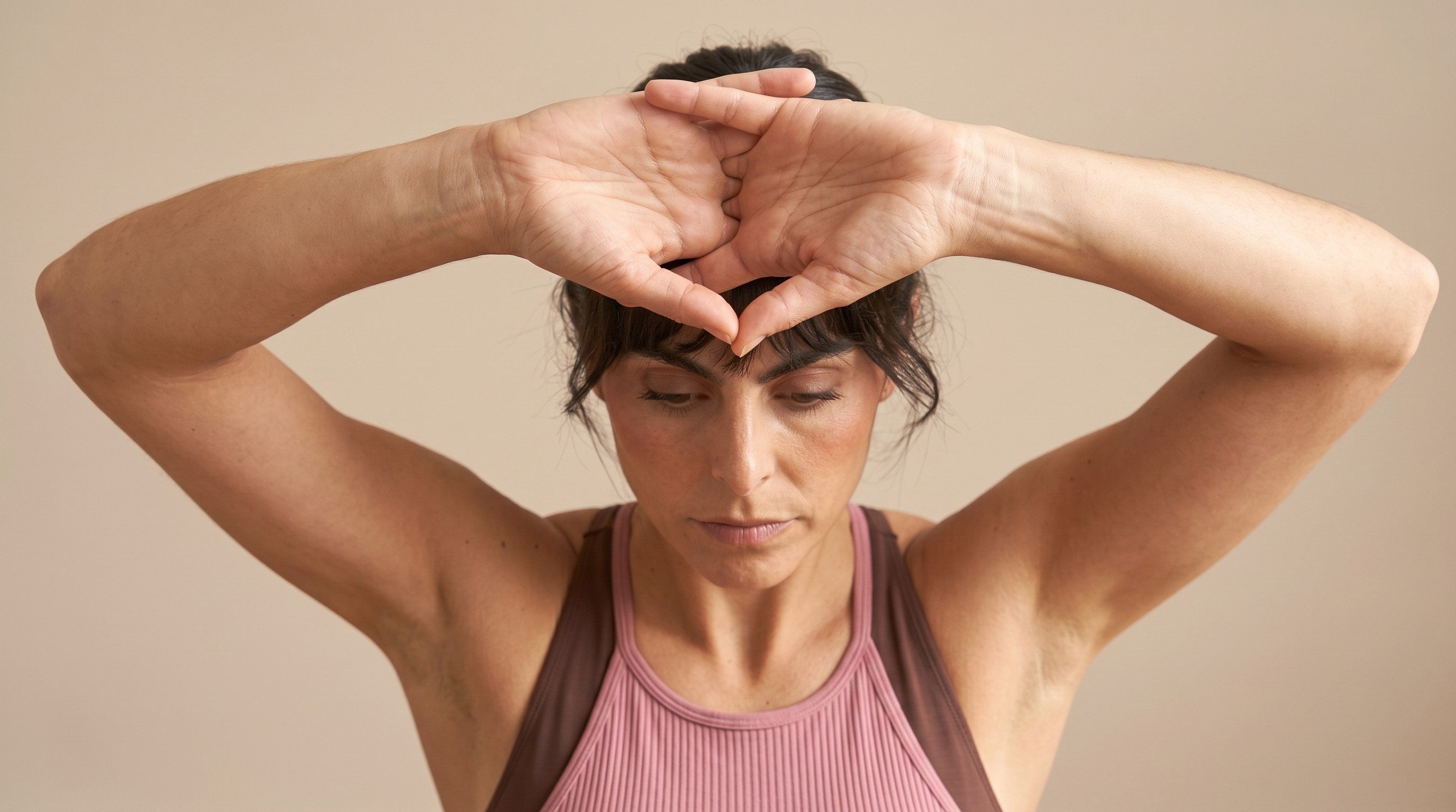 Woman in a pink tank top with her hands framing her forehead in a calm, reflective pose