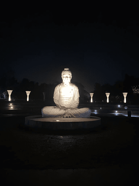 The smiling Buddha sitting in the garden surrounded by lights.