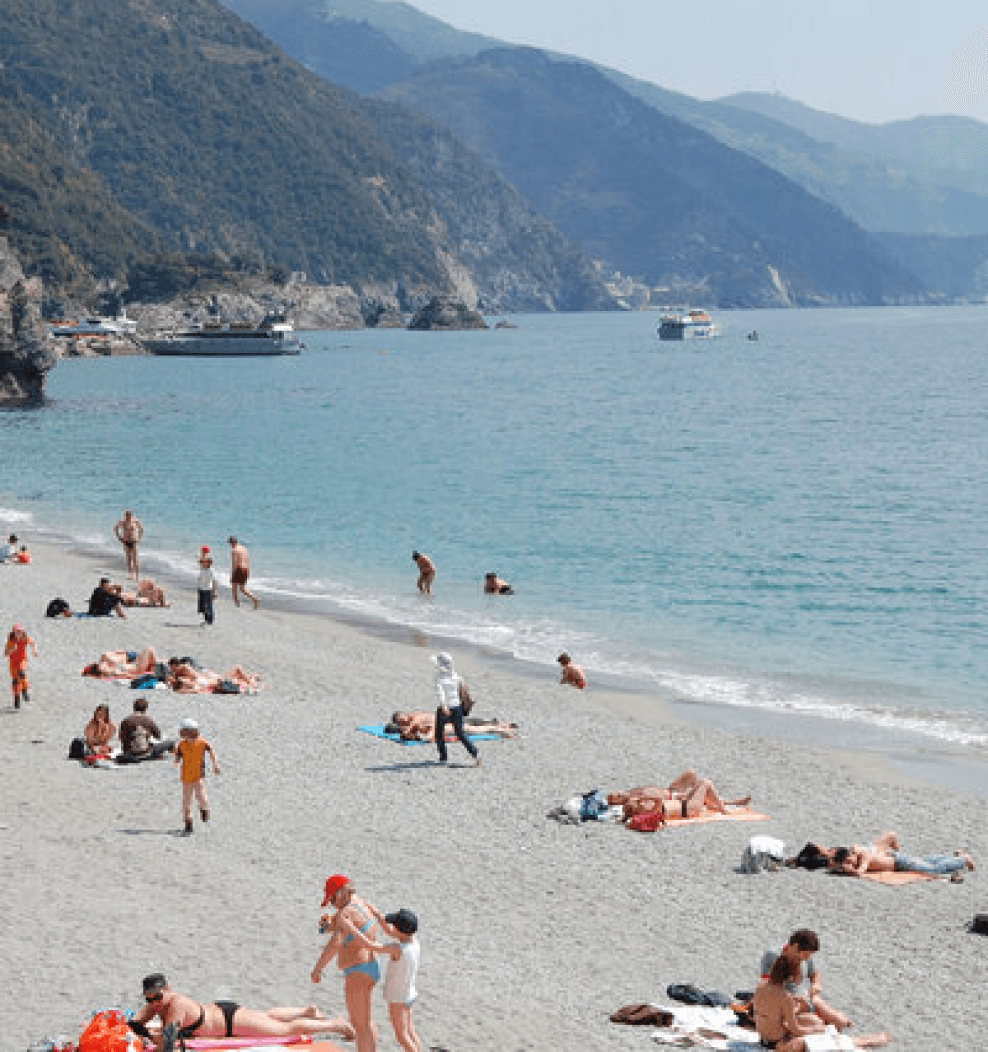 sunny beach scene with people in bright bathing suits with seaside mountains in the background