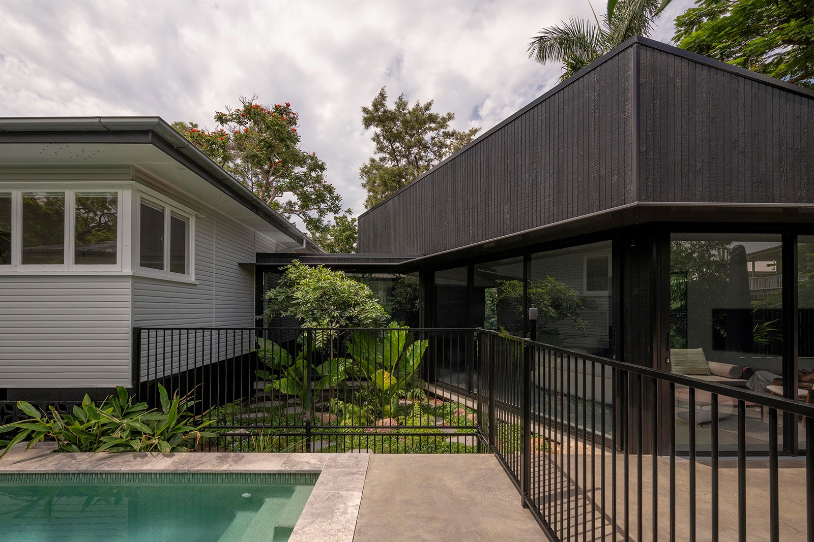 Rear pavilion and courtyard at Toohey Forest House showing contemporary black-clad addition, pool, and landscaped garden connection to original home.
