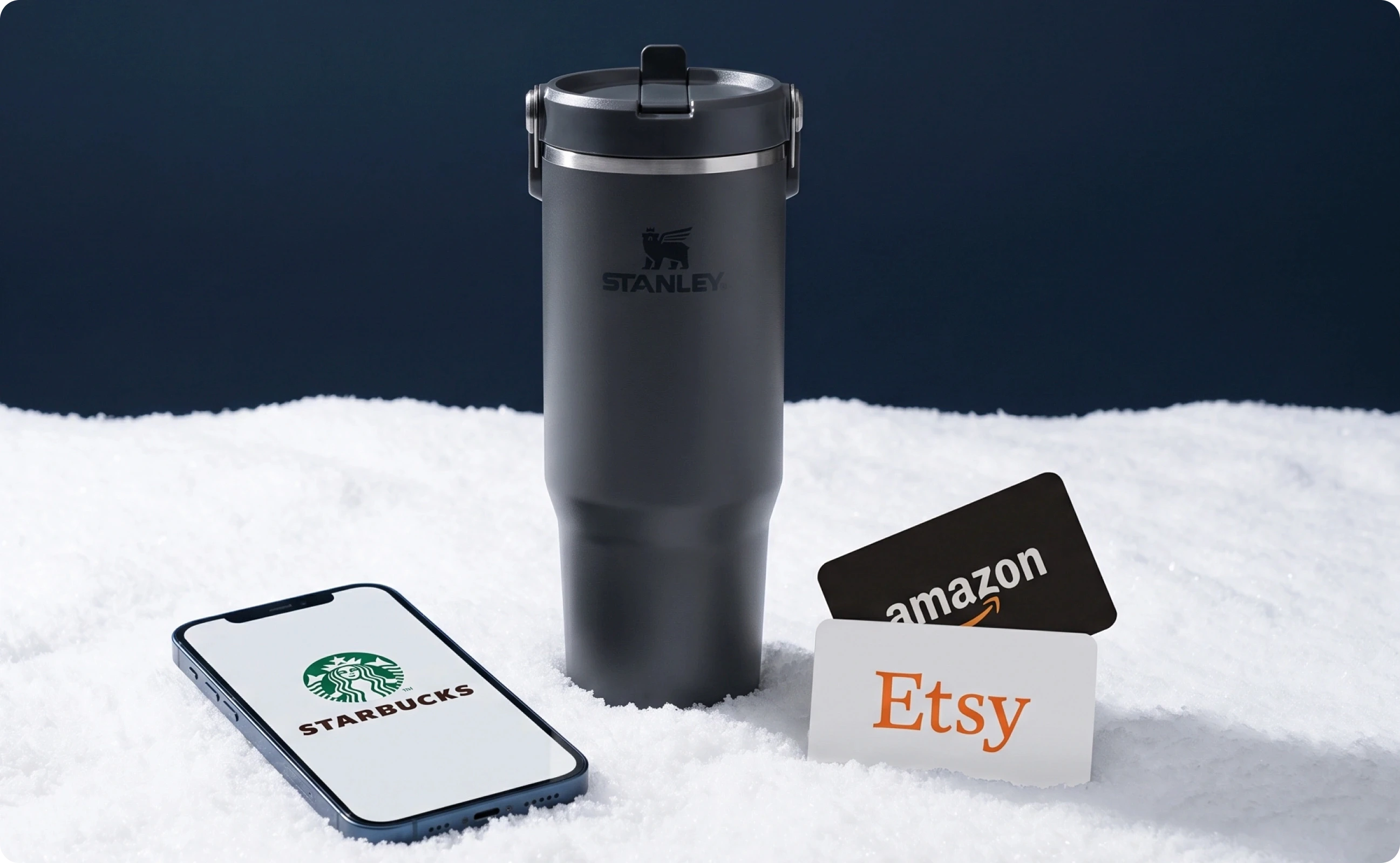A cellphone showing Stabucks, a Stanley tumbler, and gift cards atop a snowy surface.