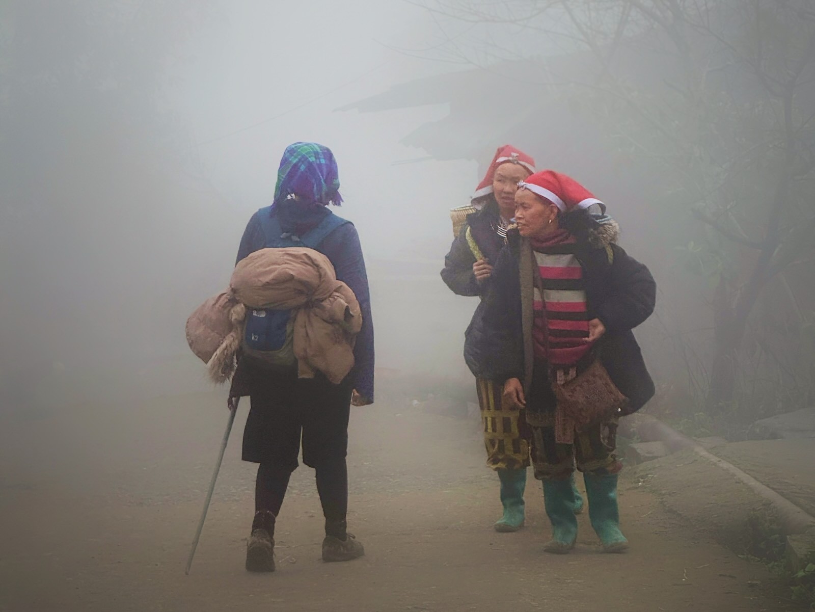 Red Dao women walking through a misty village road in Sapa meet a local Black Hmong trekking guide
