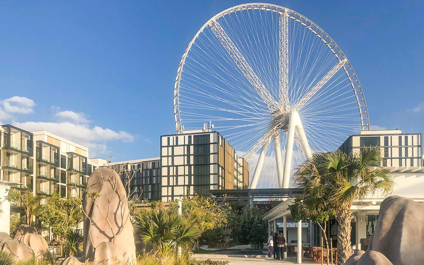 A close-up daytime view of the massive Ain Dubai Ferris wheel rising behind low-rise buildings and landscaping on Bluewaters Island.