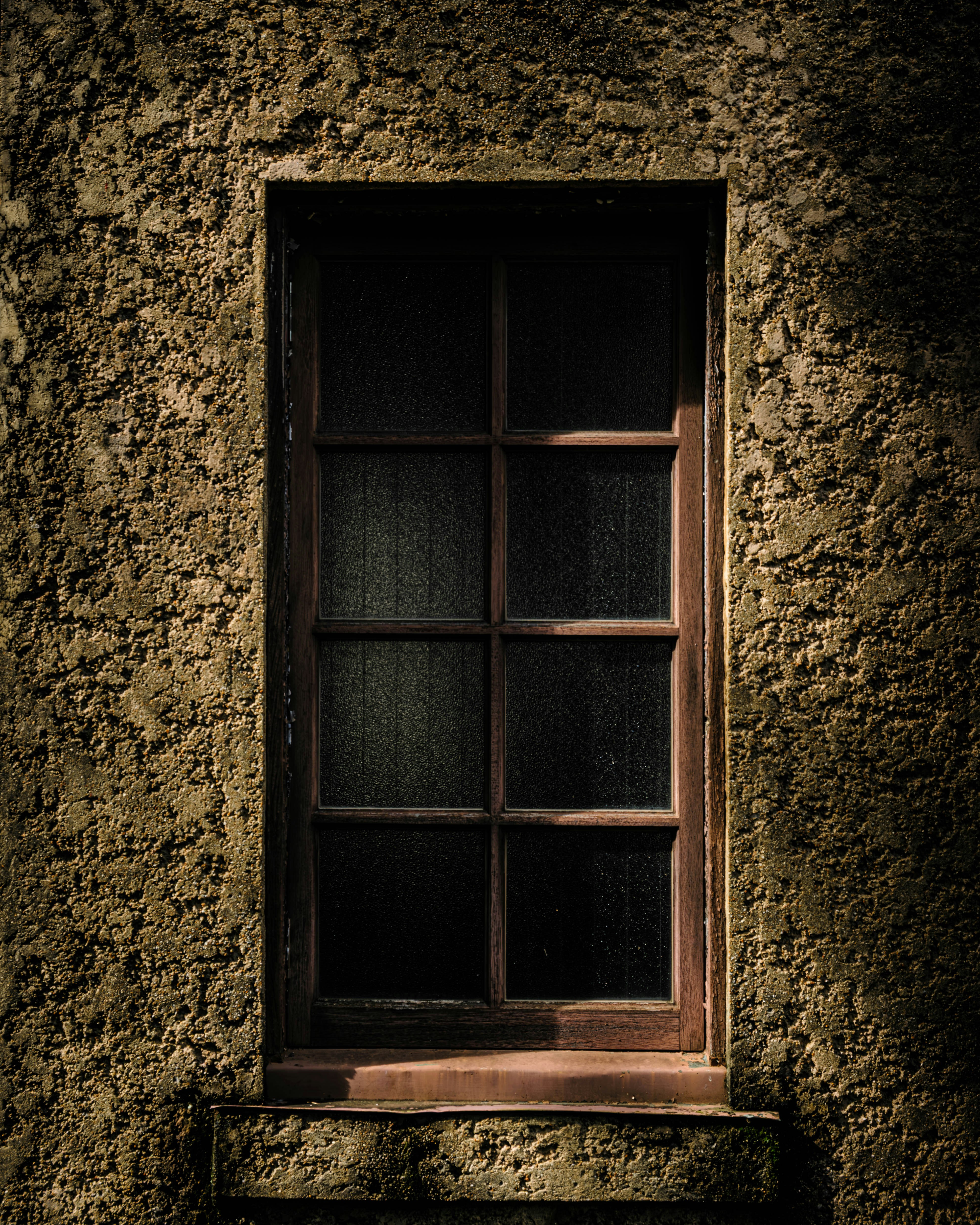 A wooden window sits in a textured wall.