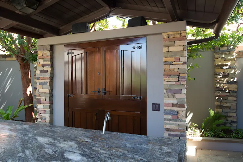Closed entertainment cabinet with custom dark stained wood doors underneath a covered patio area from the Big Canyon Remodel project. Photo by Chris Darnall.