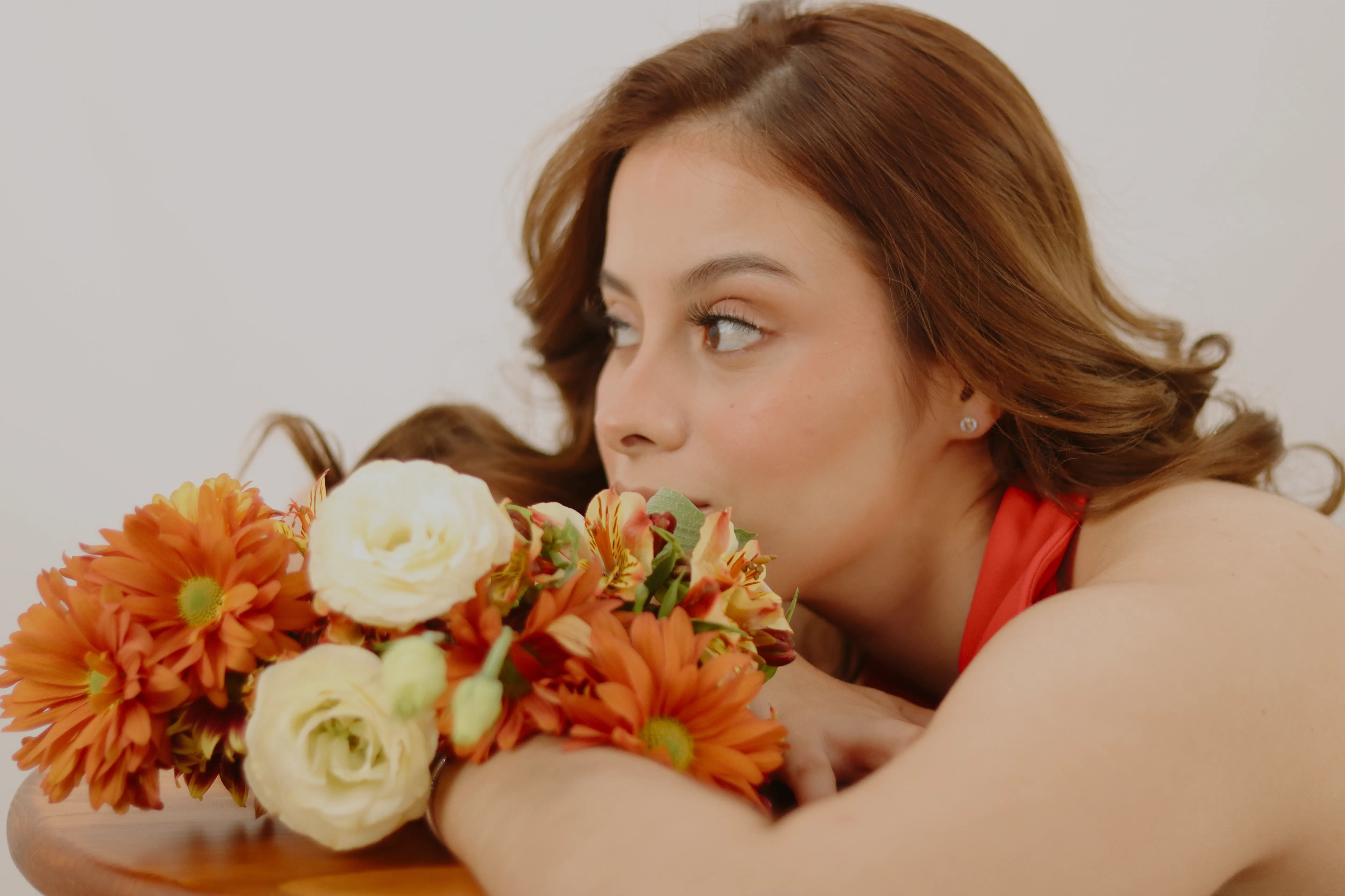 Retrato femenino con flores naranjas cerca del rostro y fondo blanco