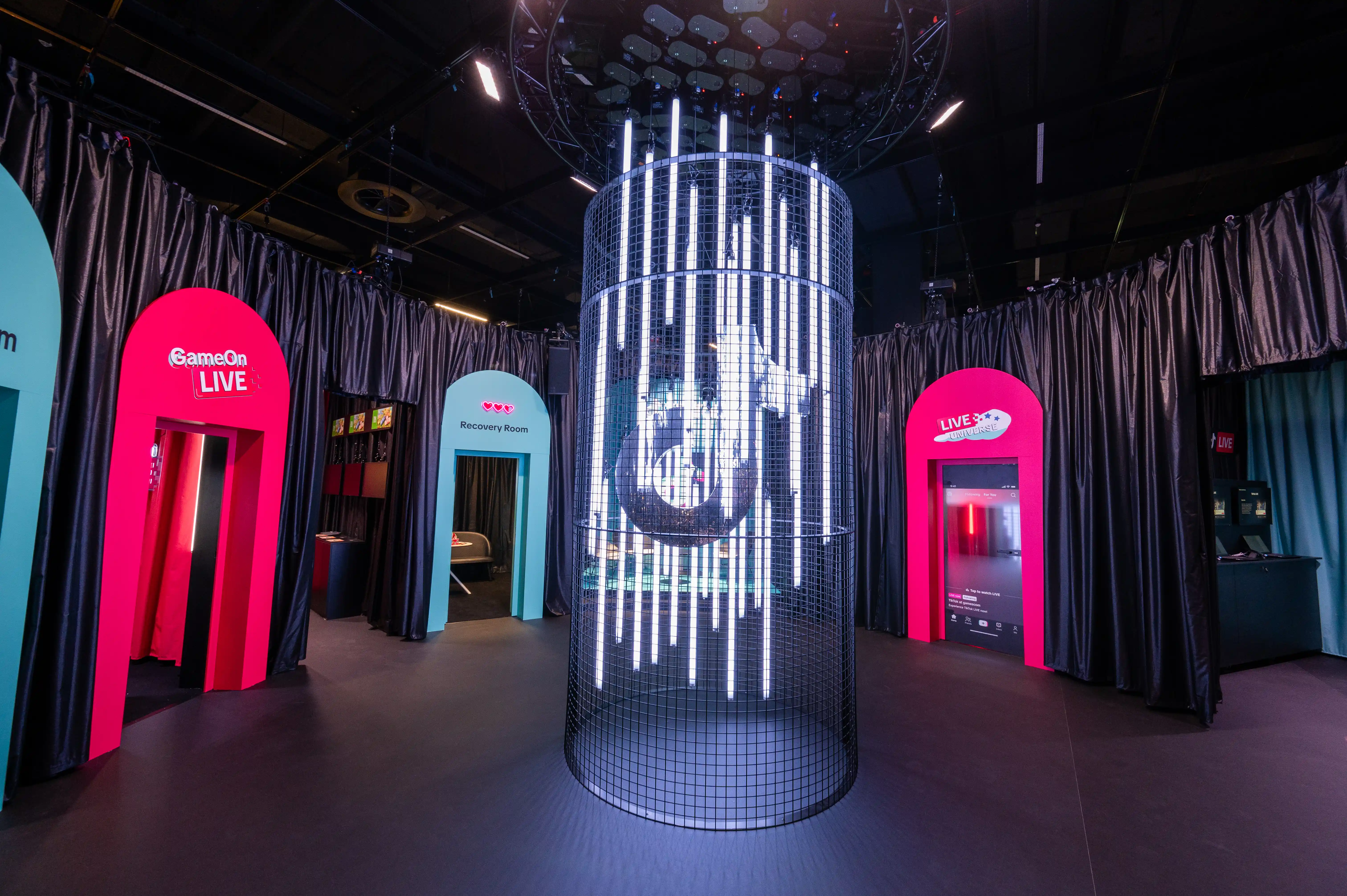 Light installation of LED rods in a wire-mesh cylinder between pink and turquoise themed portals at the TikTok booth.
