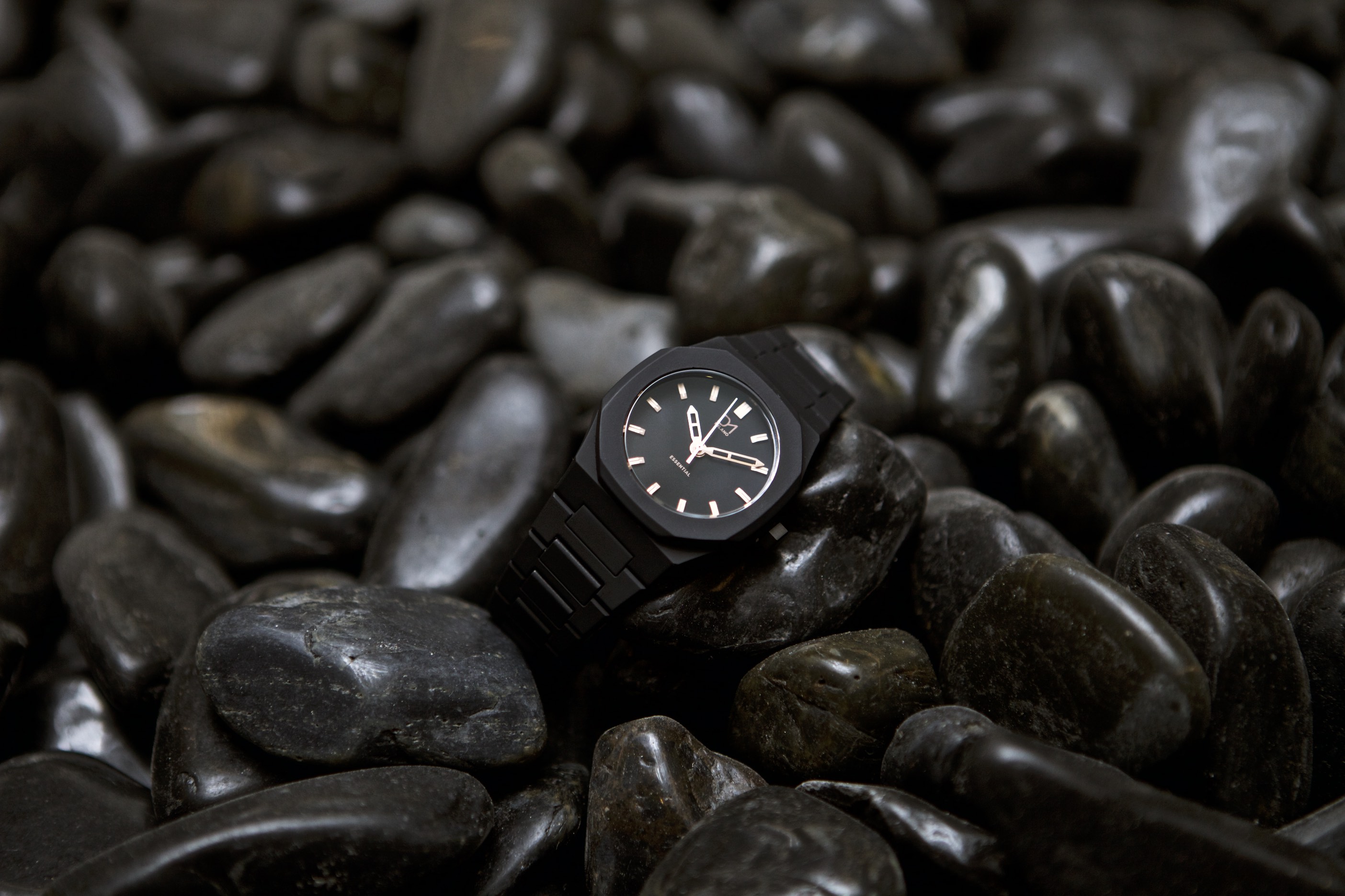 Black wristwatch resting on wet, dark stones in a close-up product shot.