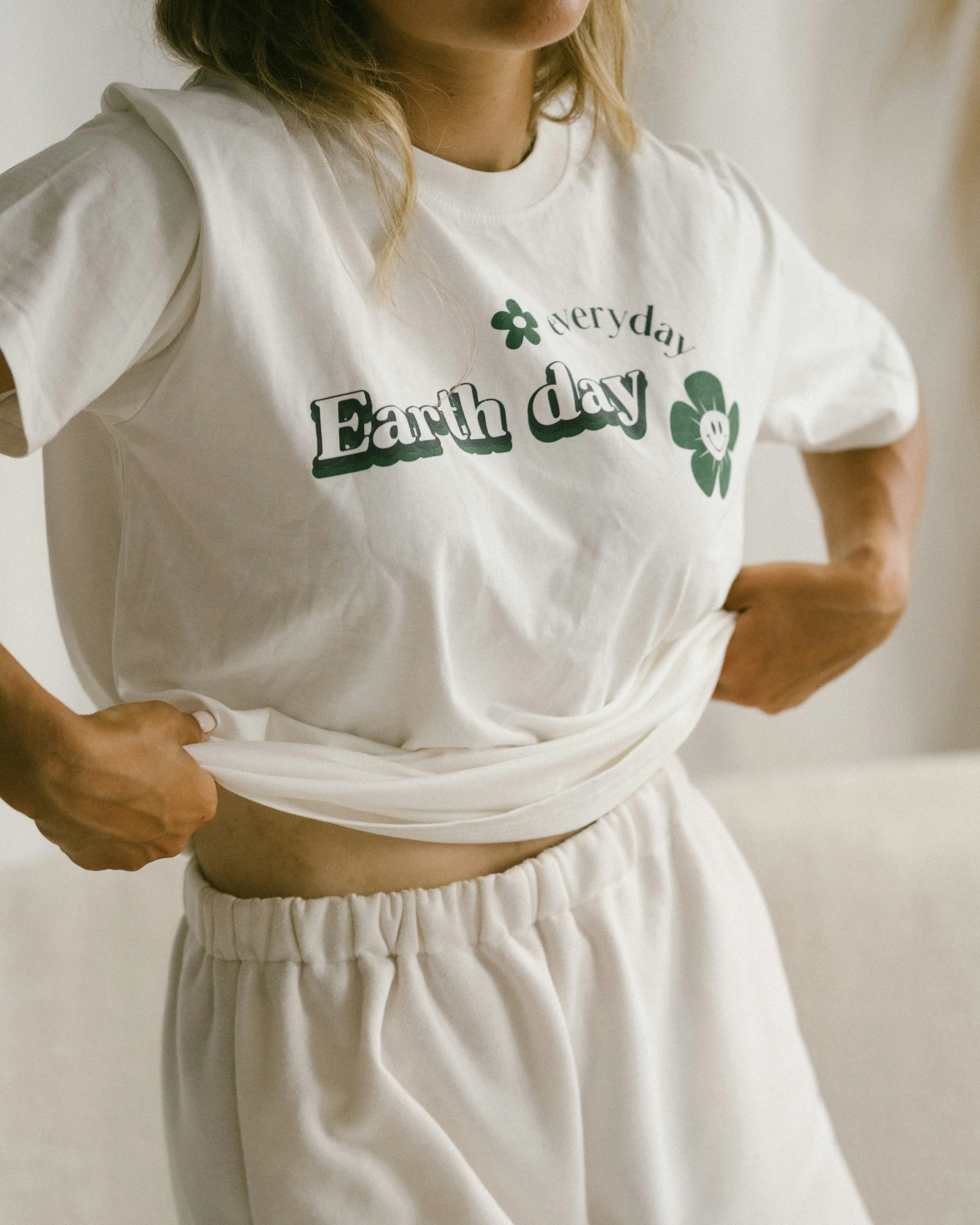 Woman putting on a white t-shirt with "Every day earth day" print.