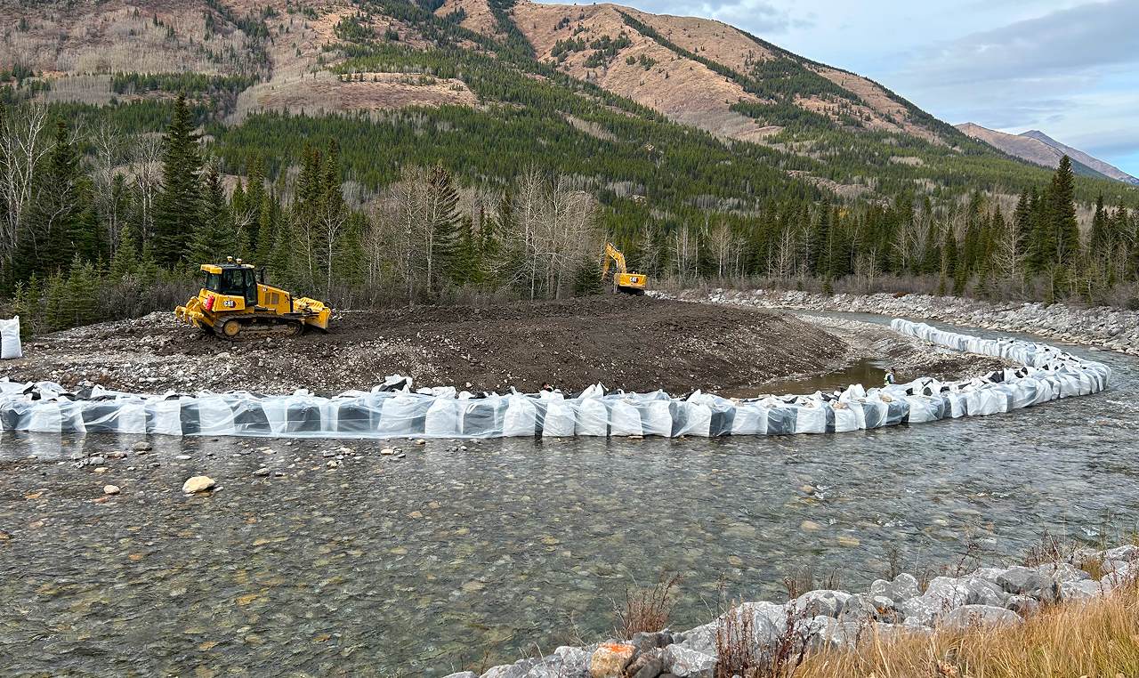 Bulldozer and excavator constructing cofferdam with supersack barriers on Kananaskis River gravel bar