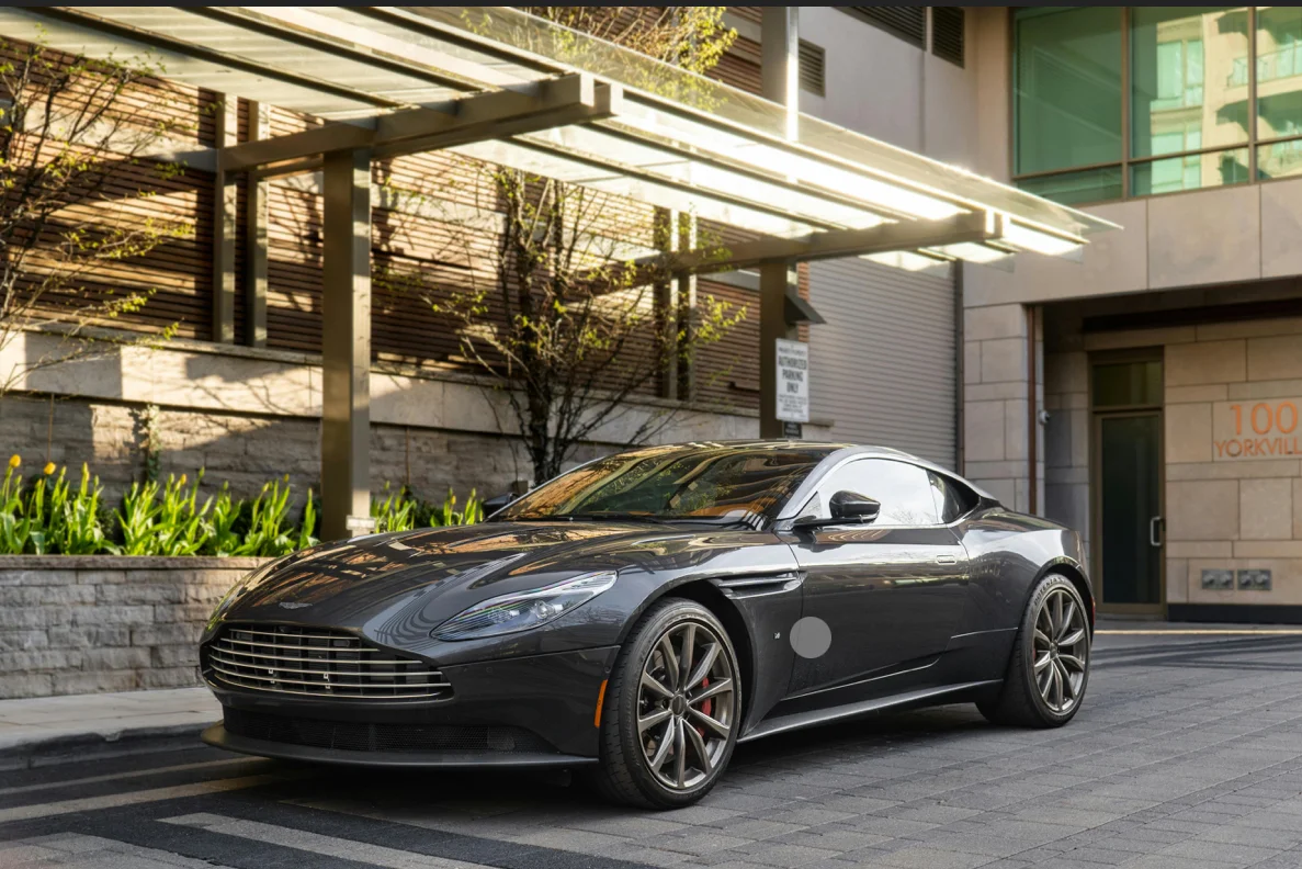 Une Aston Martin moderne stationnée devant une architecture contemporaine. Sa silhouette basse, ses lignes fluides et son élégance naturelle incarnent le luxe britannique et la sportivité raffinée, entre discrétion haut de gamme et puissance maîtrisée.