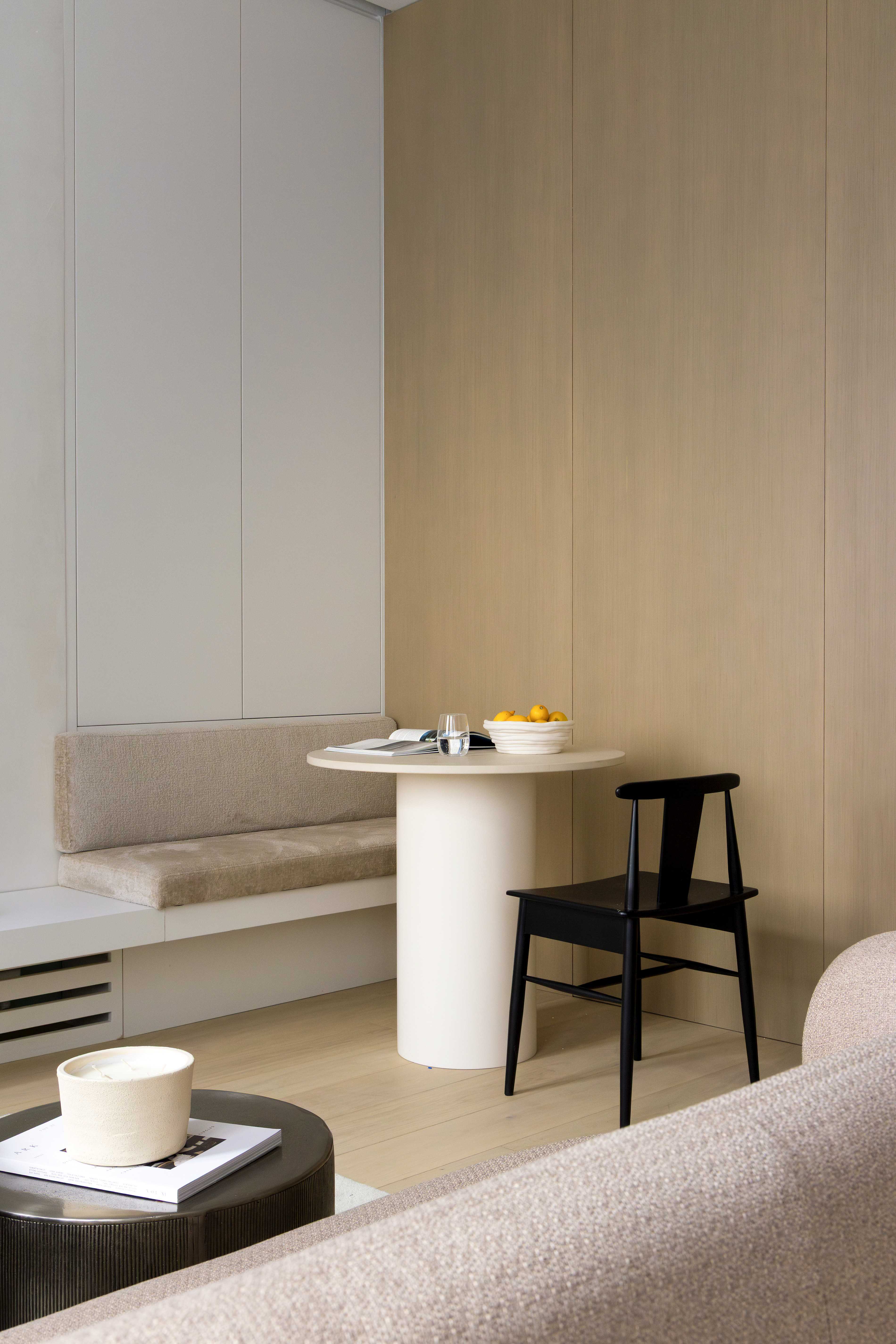 Detail du coin repas avec banquette velours beige, table ronde blanche avec agrumes, chaise noire et canape en premier plan
