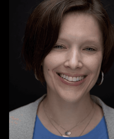 Editorial portrait of a young man with wavy hair in a knit sweater, looking over his shoulder in soft light.