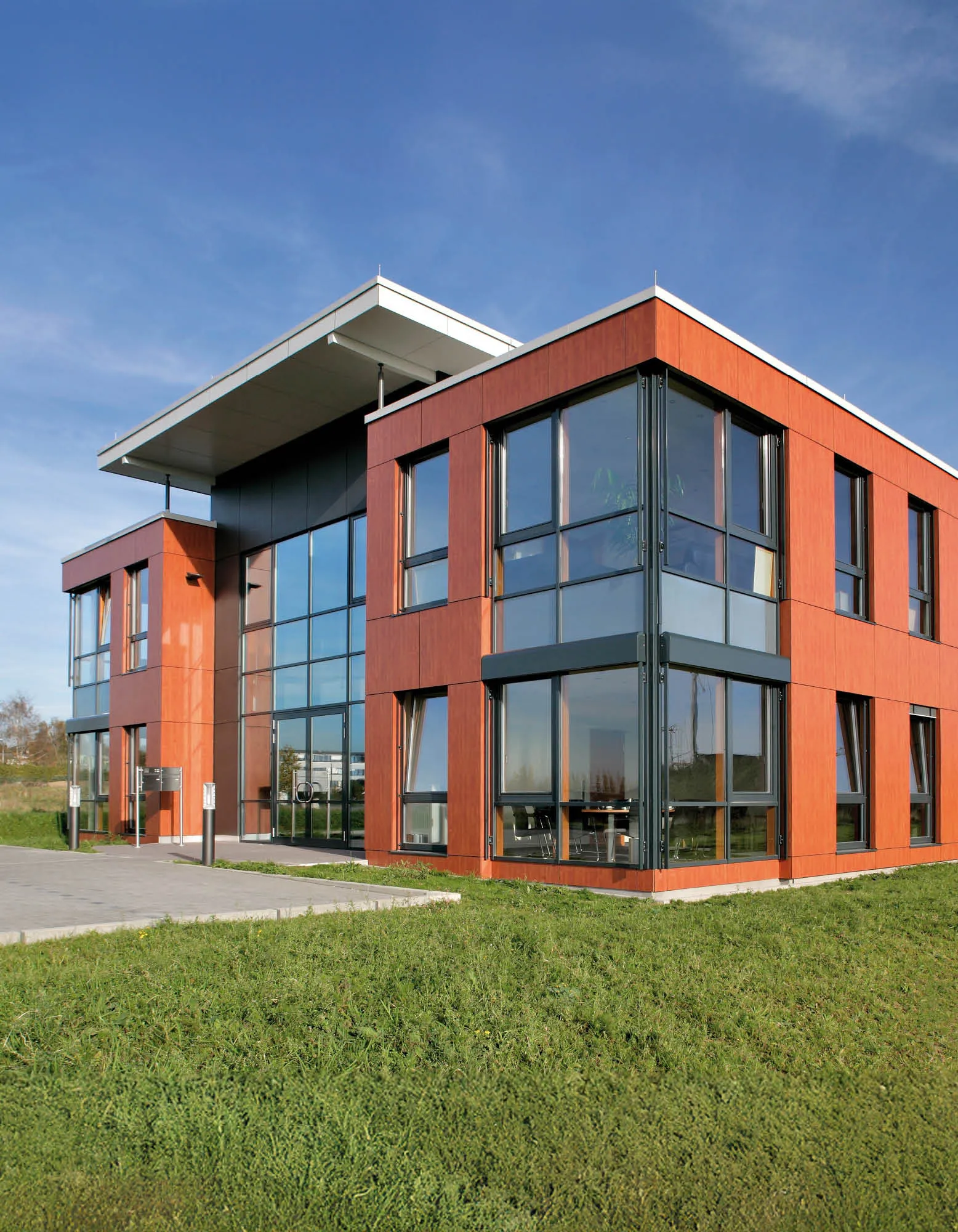 Modernes Bürogebäude mit Holzfassade und großzügigen Glasflächen im strahlenden Sonnenschein vor blauem Himmel.