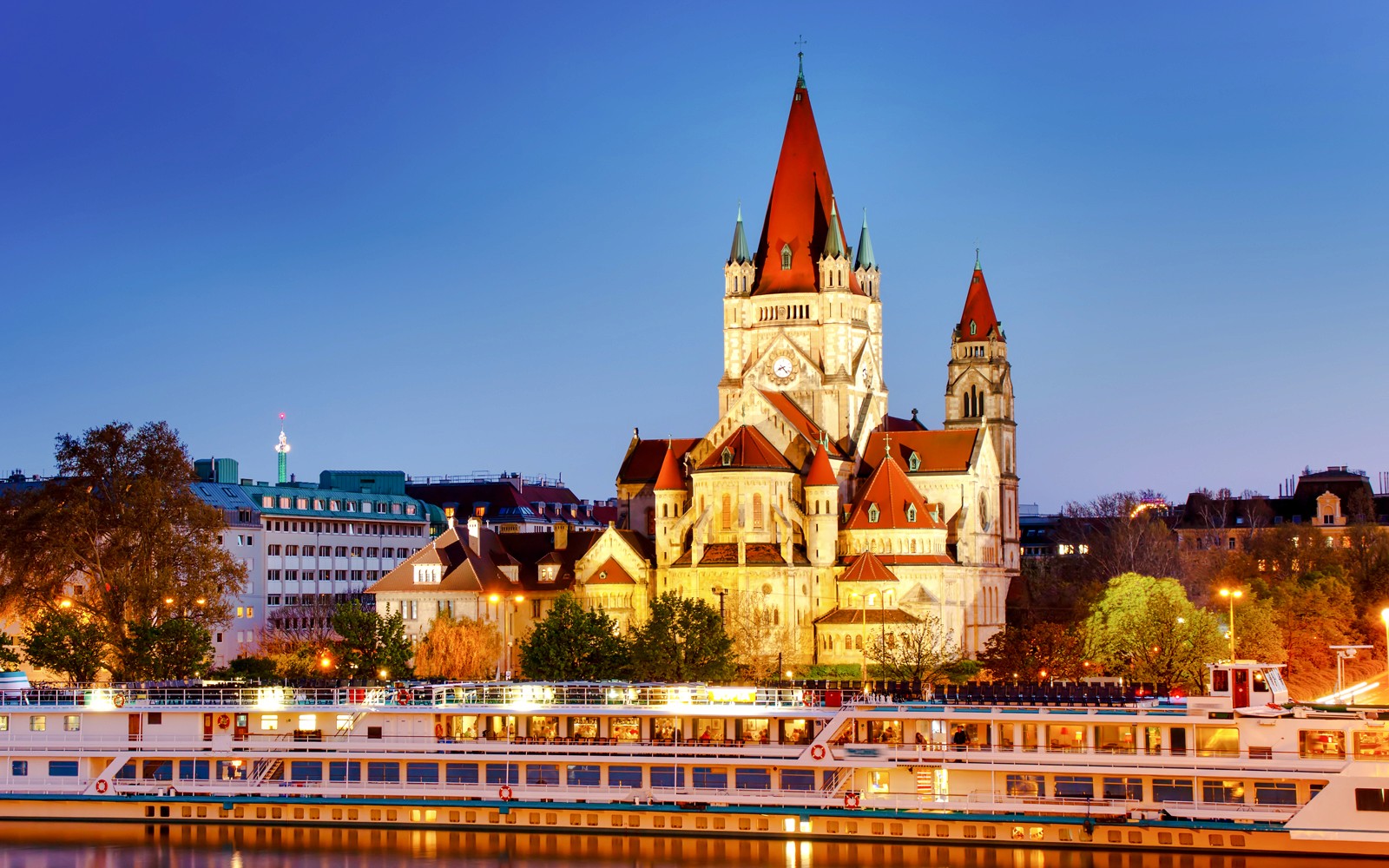 Risteilyalus Tonavalla St. Franciscus Assisilaisen kirkon kanssa Wienissä iltahämärässä.