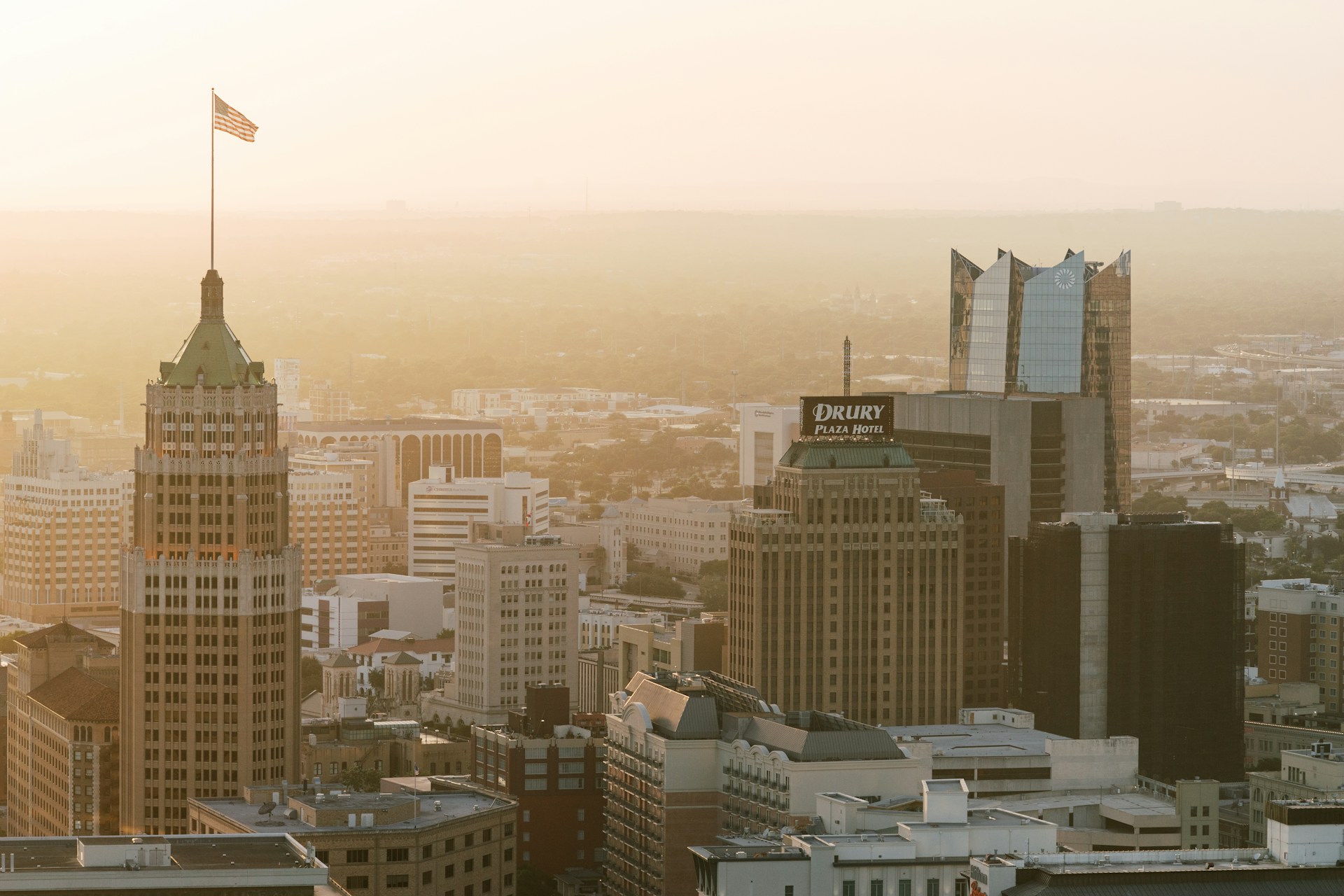 Downtown office towers bathed in warm golden morning light with an American flag atop one building.