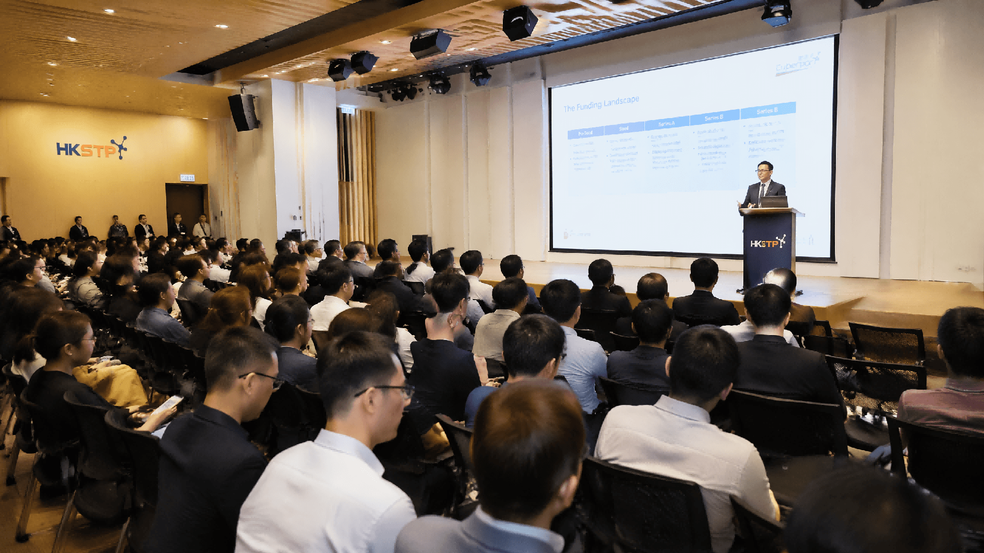 香港大型商務研討會現場，專業演講者向滿座觀眾進行投資路演及產品推廣簡報。Logo設計 香港機場零售品牌標誌設計 Airport brand logo design for Hong Kong airport retail