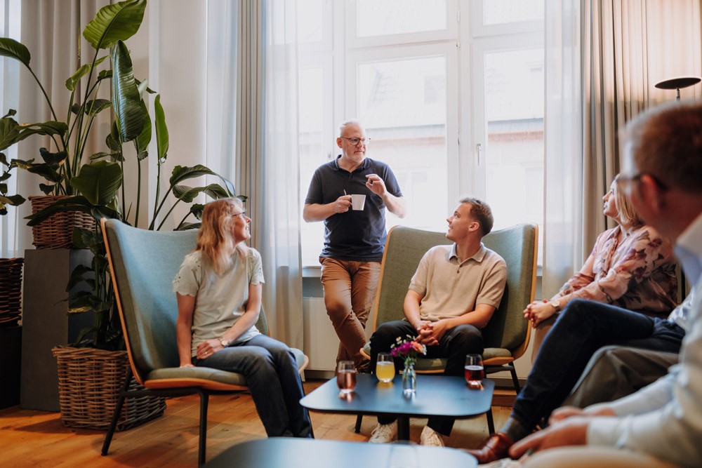 Gruppe von Personen sitzt in einer Besprechungsrunde mit mehreren Sesseln und diskutiert im hellen Raum.